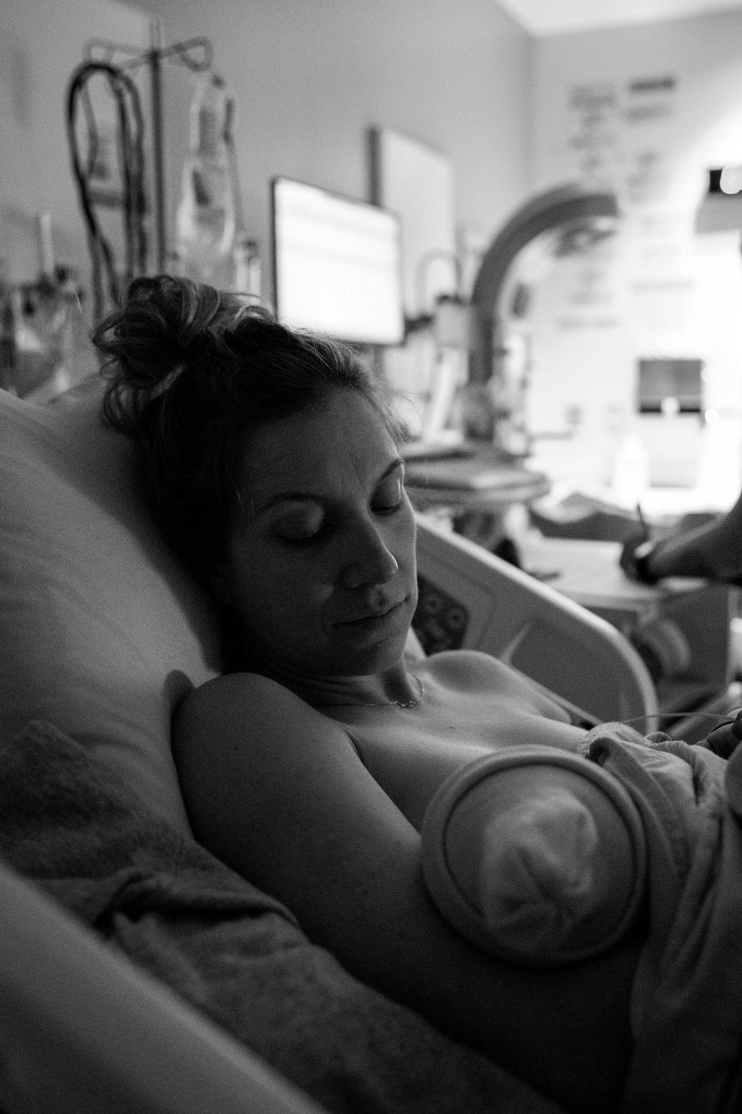 Black and white photo of a mother resting in a hospital bed while cuddling with her newborn baby.