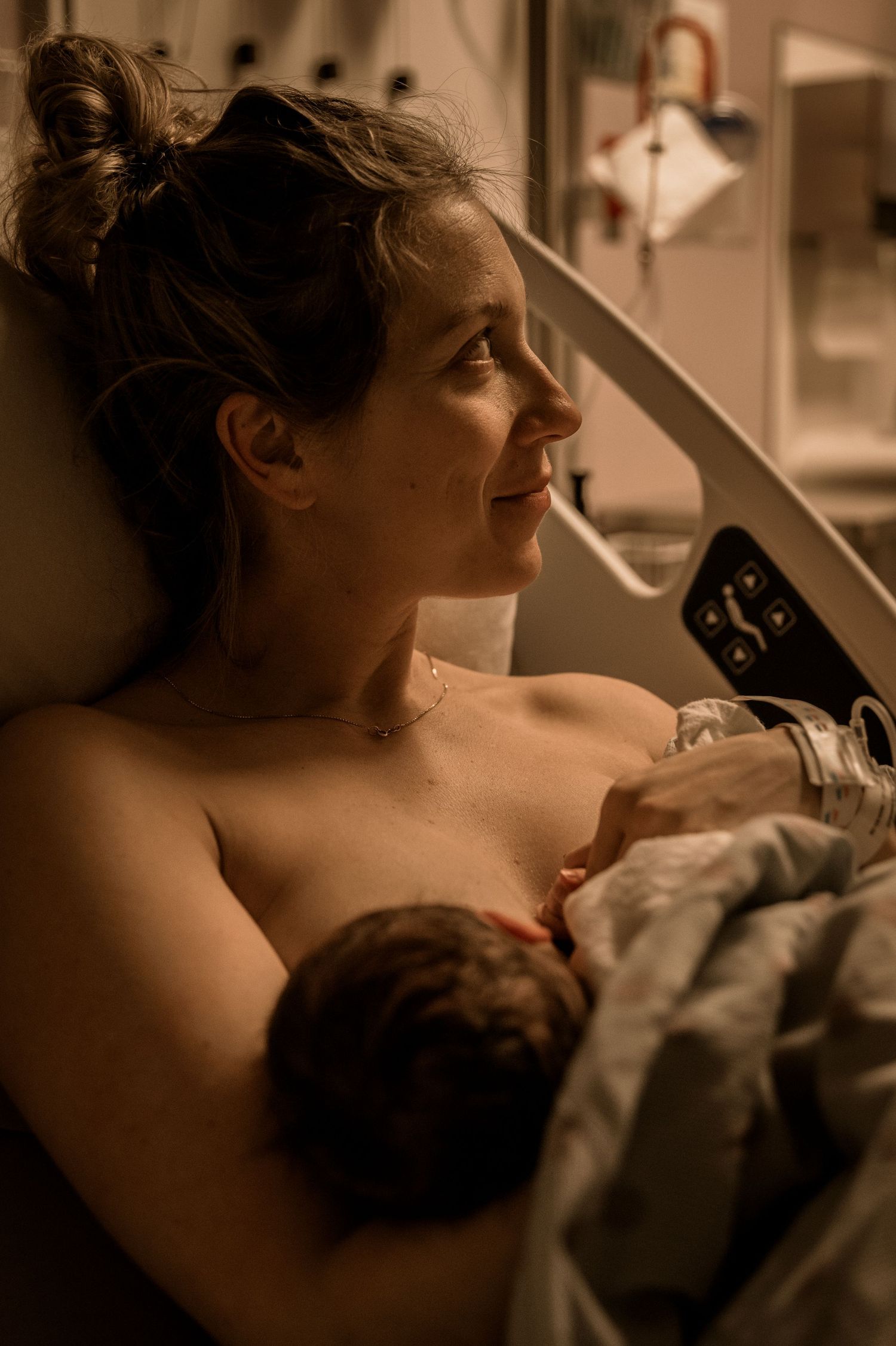 A tender moment captured in warm lighting as a new mother breastfeeds her newborn baby in a hospital room.