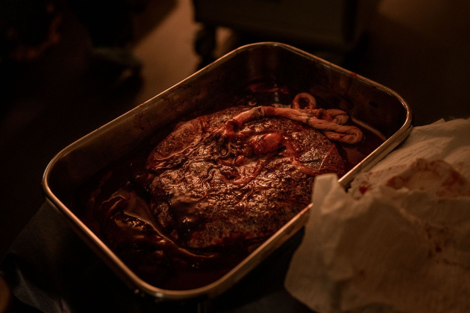 Dark roasted pot roast with carrots and rich gravy in a black roasting pan under warm lighting.