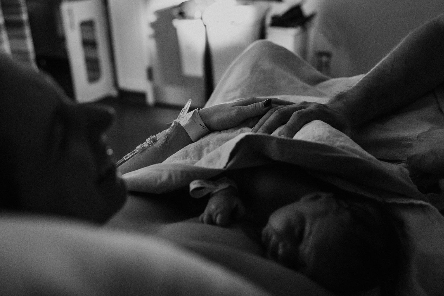 Black and white photo showing someone sleeping under grey blankets in dim lighting conditions.