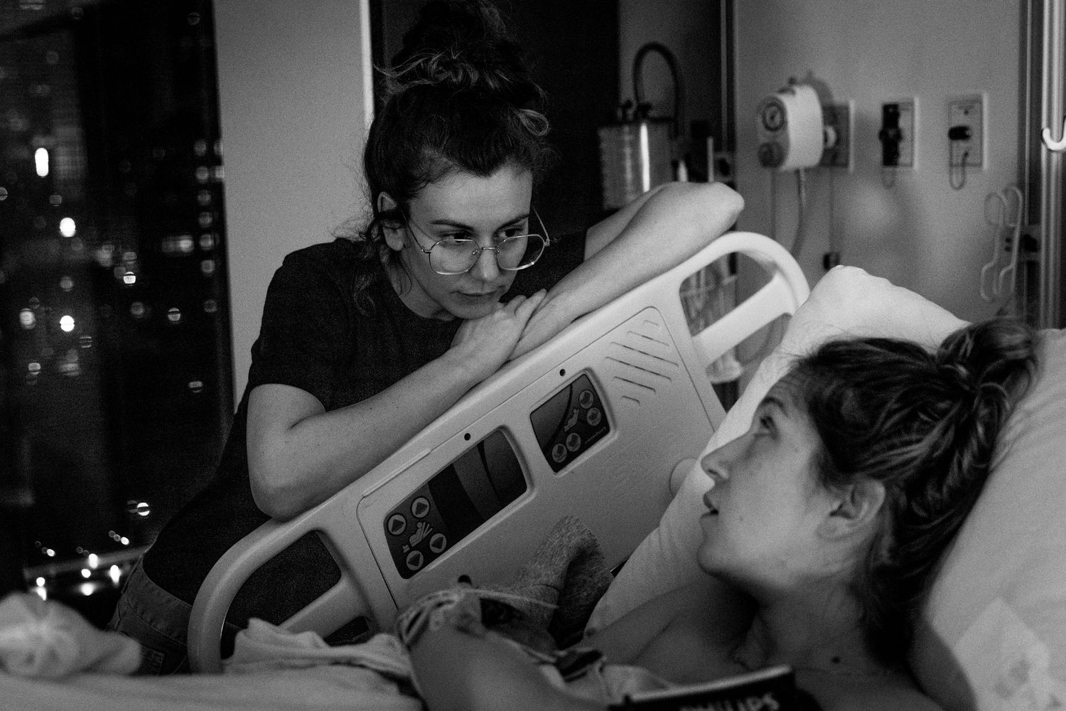 Black and white photograph of two individuals in a hospital room with medical equipment visible in the dark.