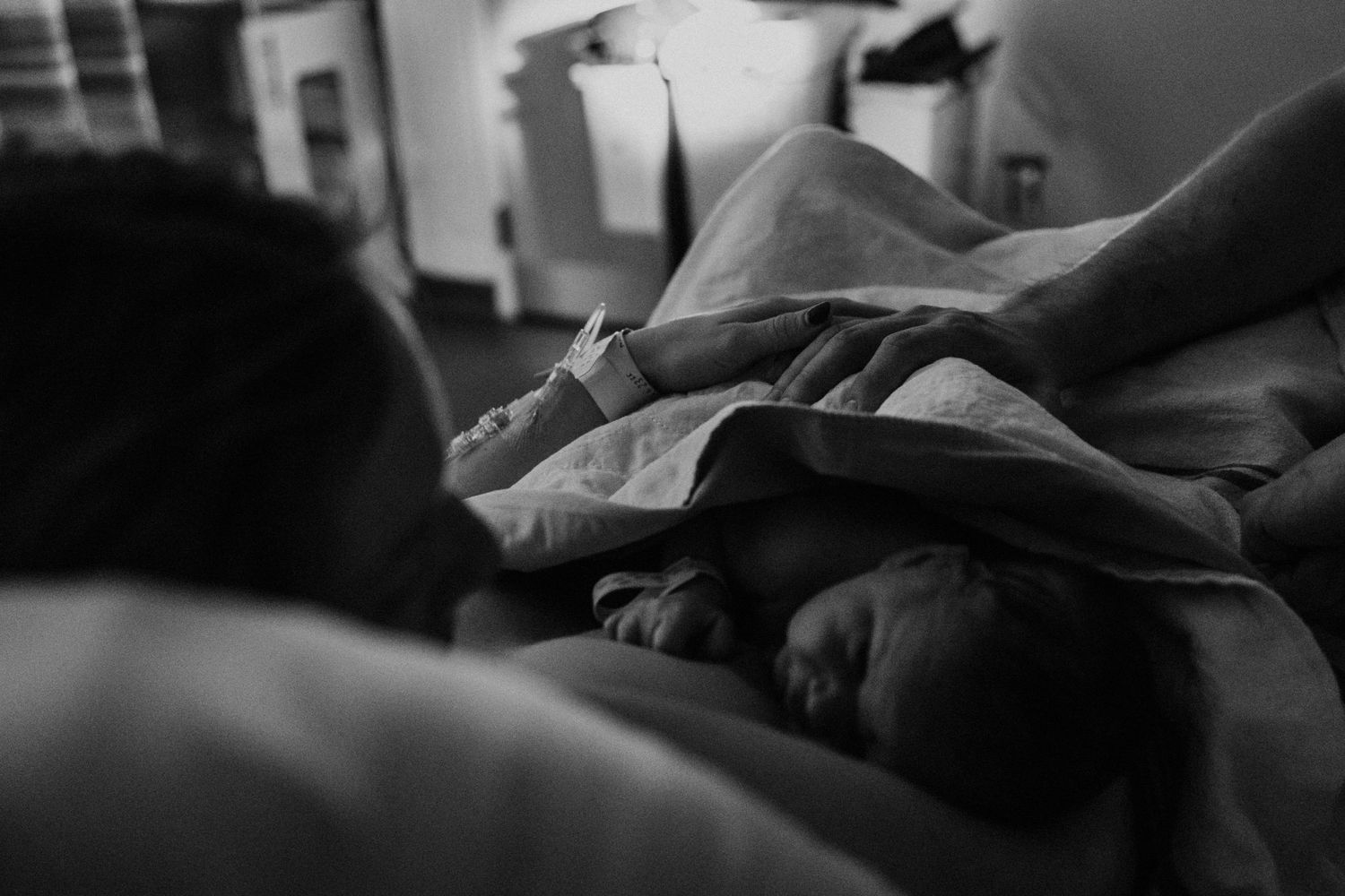 Black and white moody photo of someone resting under blankets in bed, shot from a low angle.