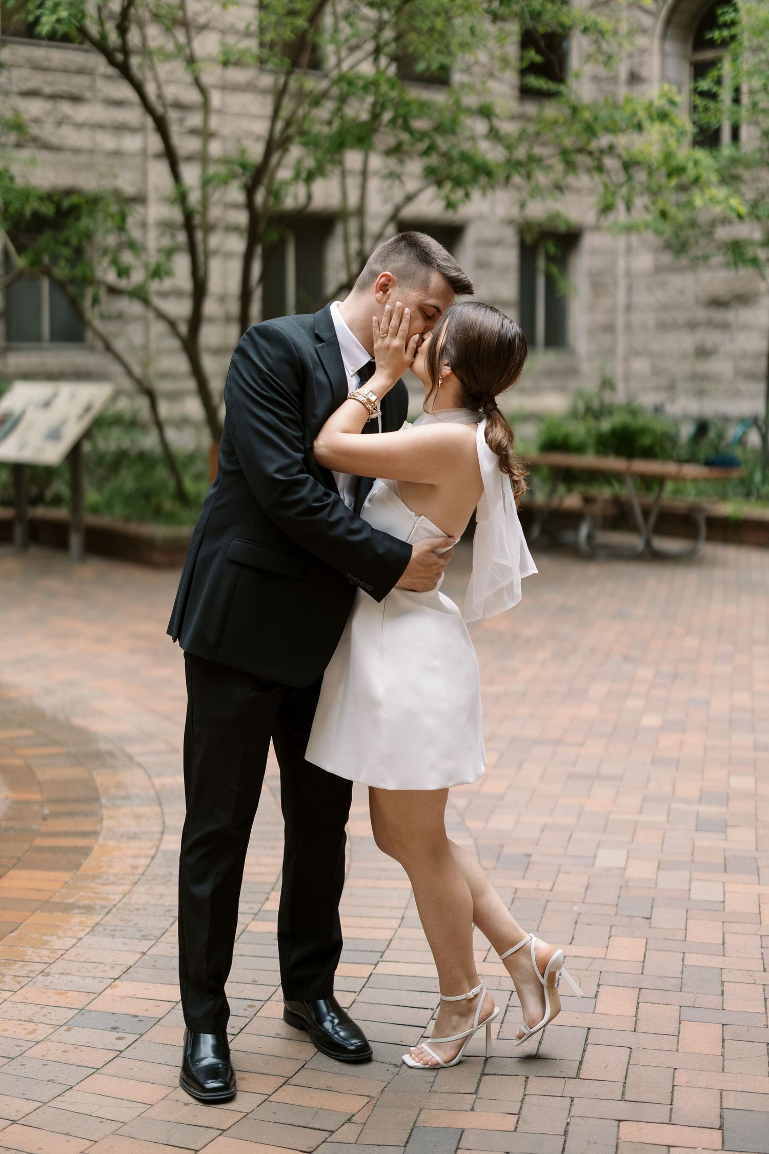 A romantic moment between a couple in formal attire on a brick courtyard.