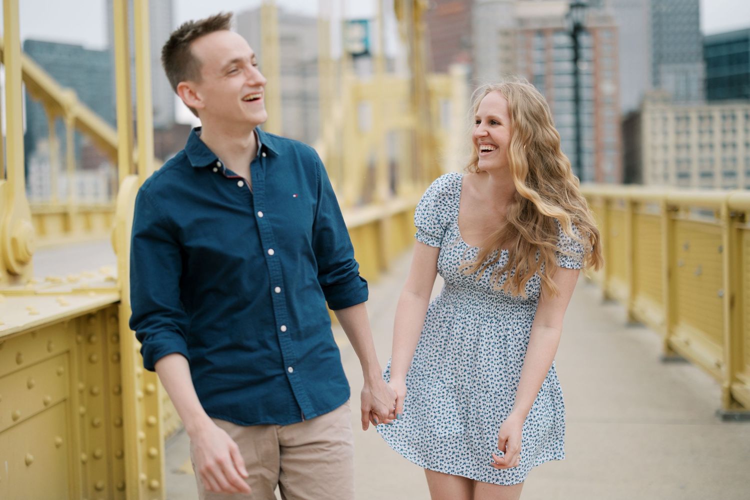 Couple in casual attire laughing while walking on yellow bridge.