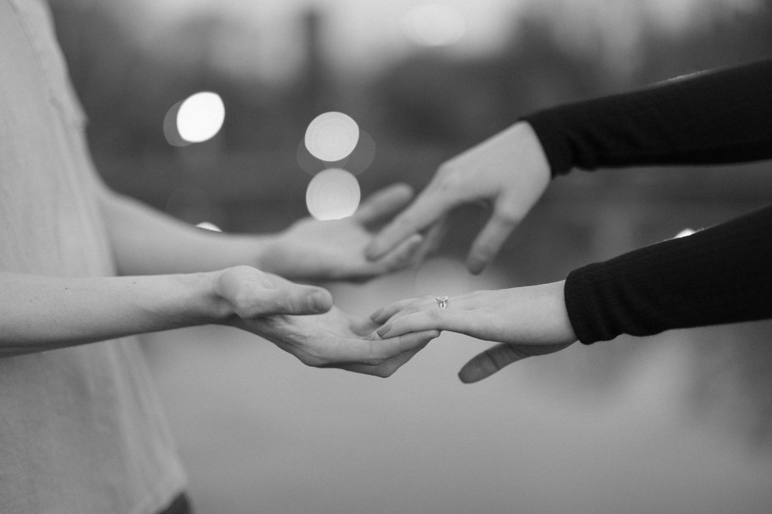 Black and white close-up of hands touching tenderly in soft focus.