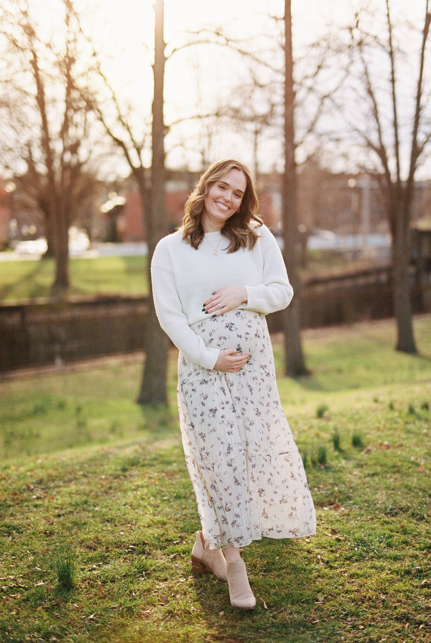 A woman in a floral dress poses gracefully across a series of outdoor photos at sunset in a grassy park setting.