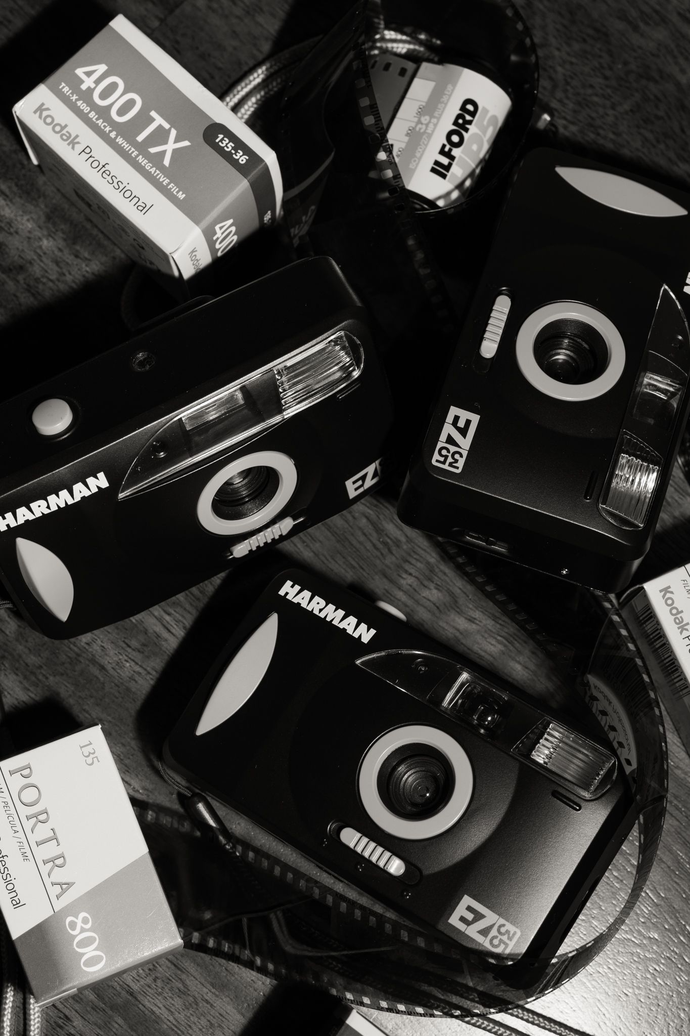 Black and white collection of analog film rolls and vintage camera equipment scattered on a dark surface.