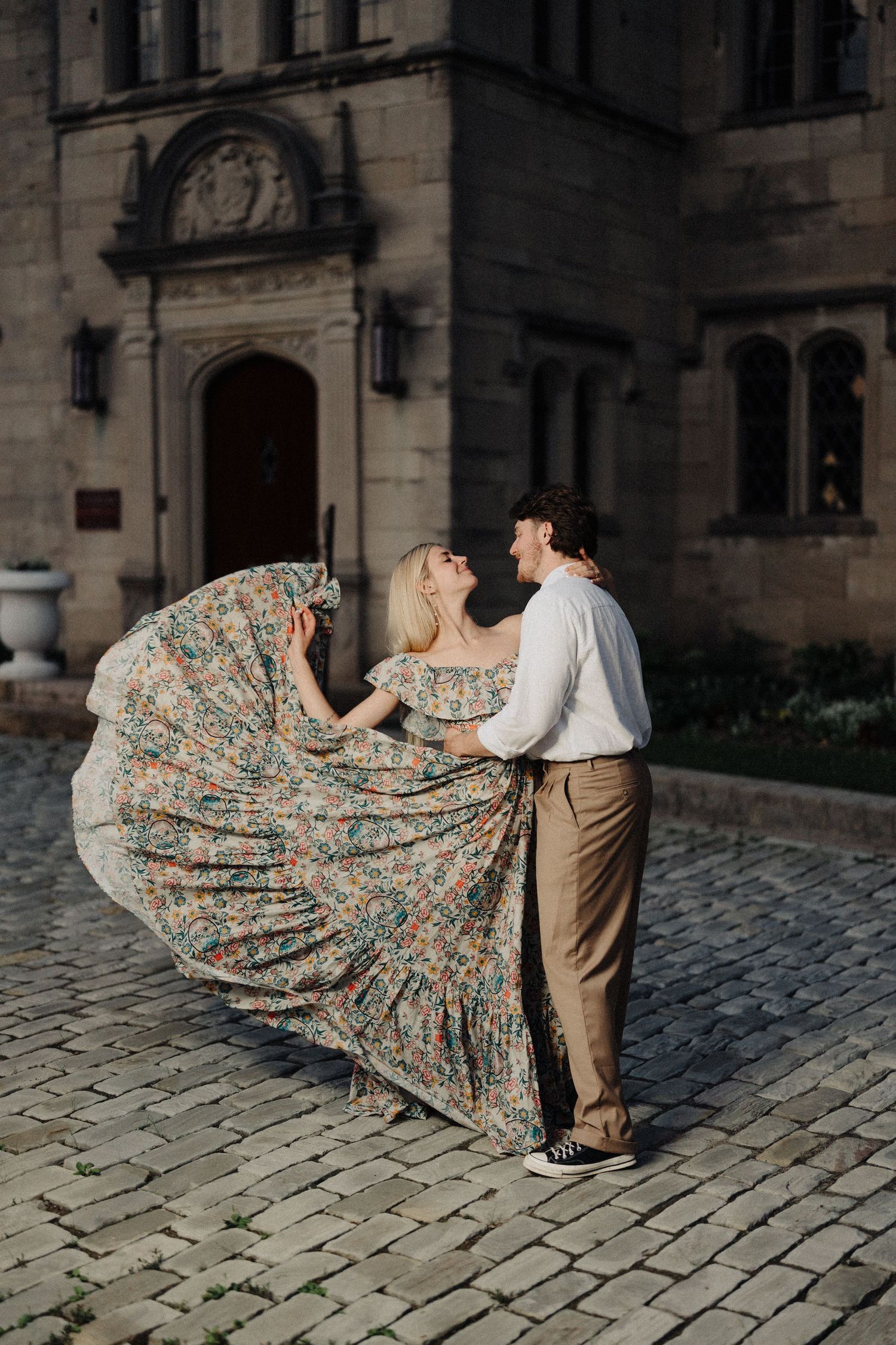 A couple dances outdoors as her floral dress twirls dramatically against historic architecture.