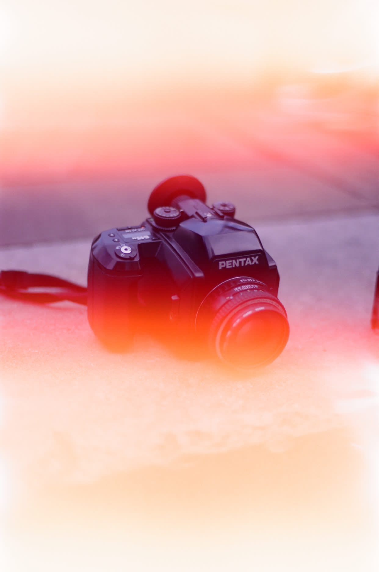 Pentax camera with lens against dreamy pink and orange sunset background.