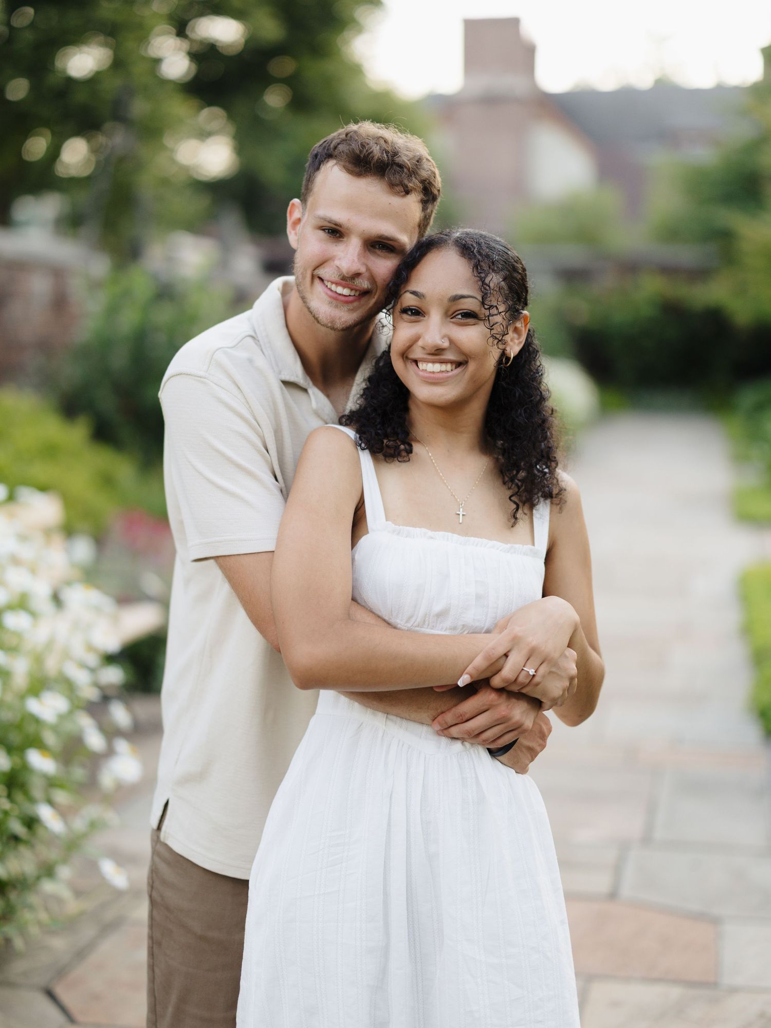A couple in casual white and beige outfits embrace outdoors while sharing joyful moments together.