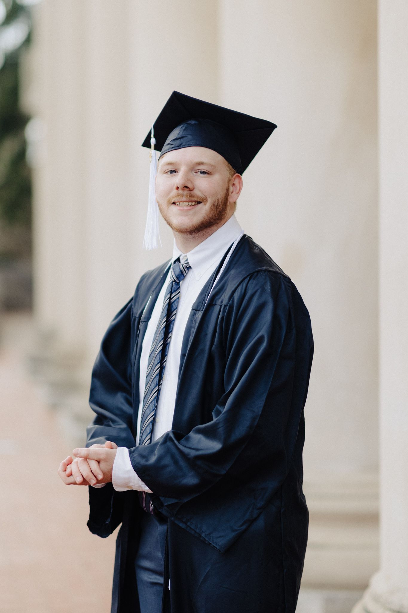 Graduate in traditional academic regalia smiles warmly in front of classical columns.