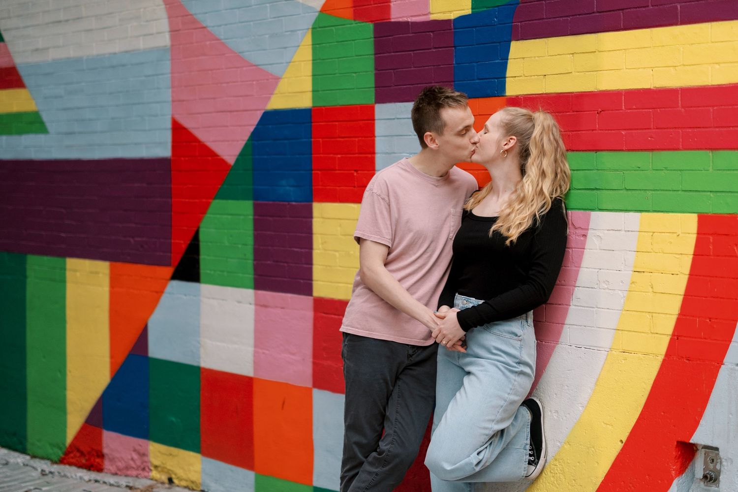 A romantic moment captured against a vibrant geometric wall mural in an urban setting.