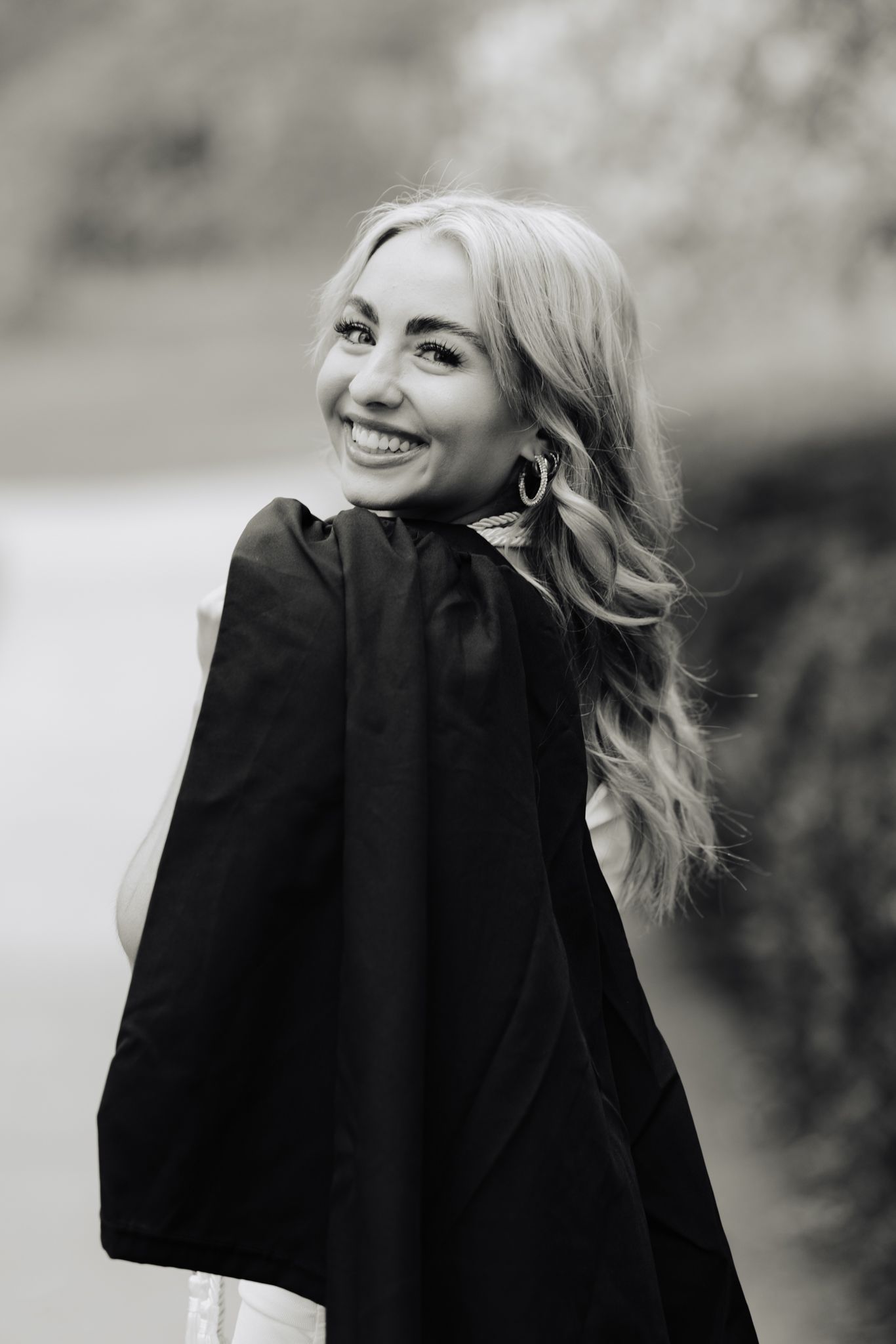 Black and white portrait captures graduate's joyful smile in academic regalia.
