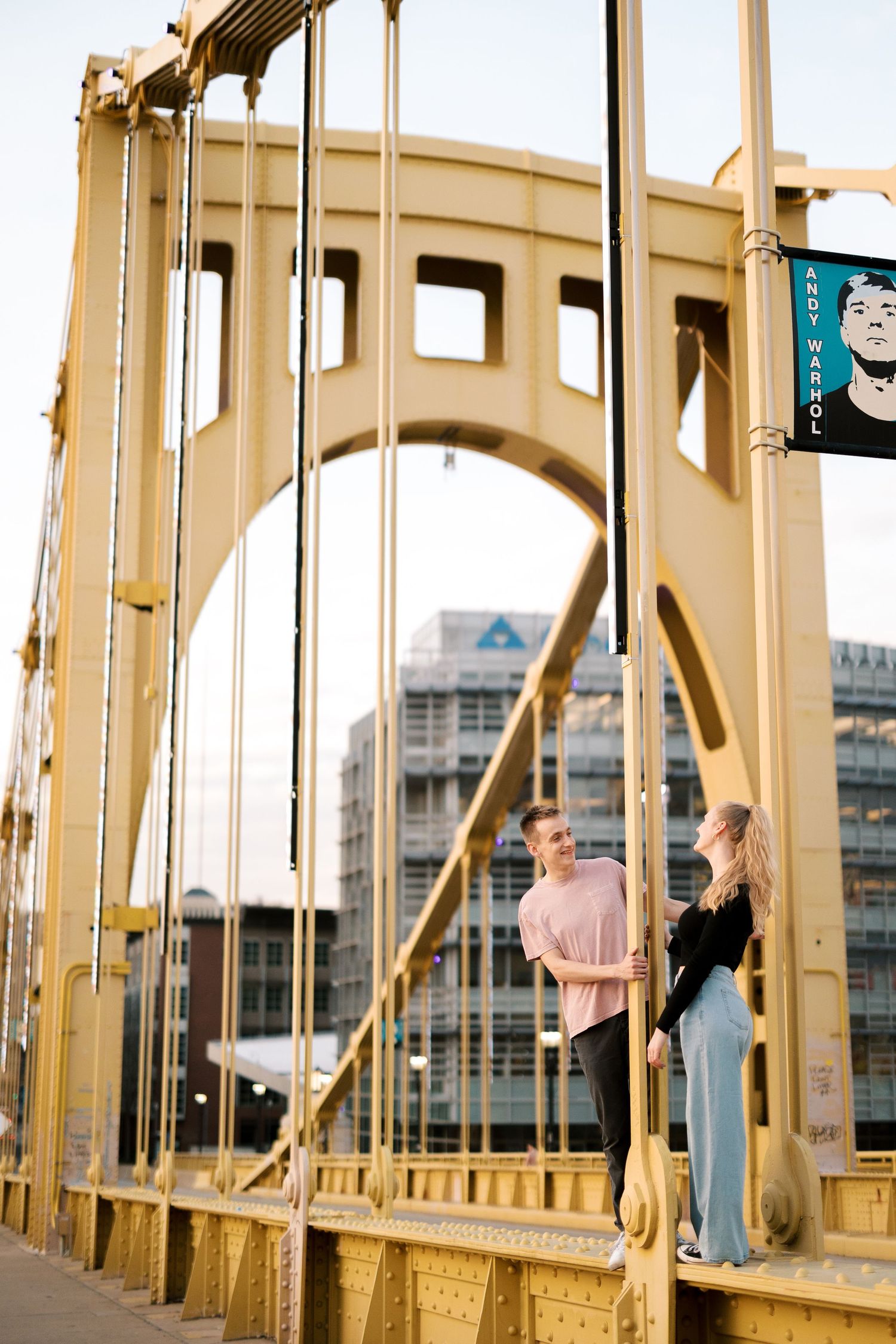 A couple standing on the iconic yellow Roberto Clemente Bridge in Pittsburgh at sunset.