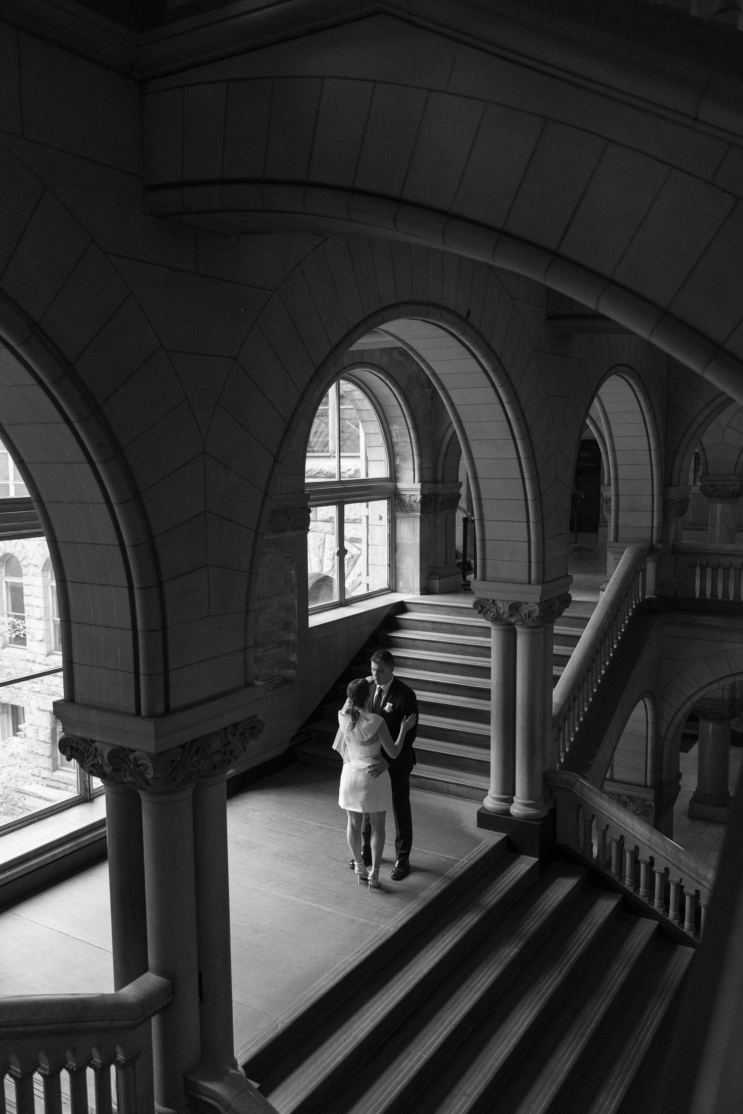 A black and white photograph showing a couple in an architecturally stunning stairwell.