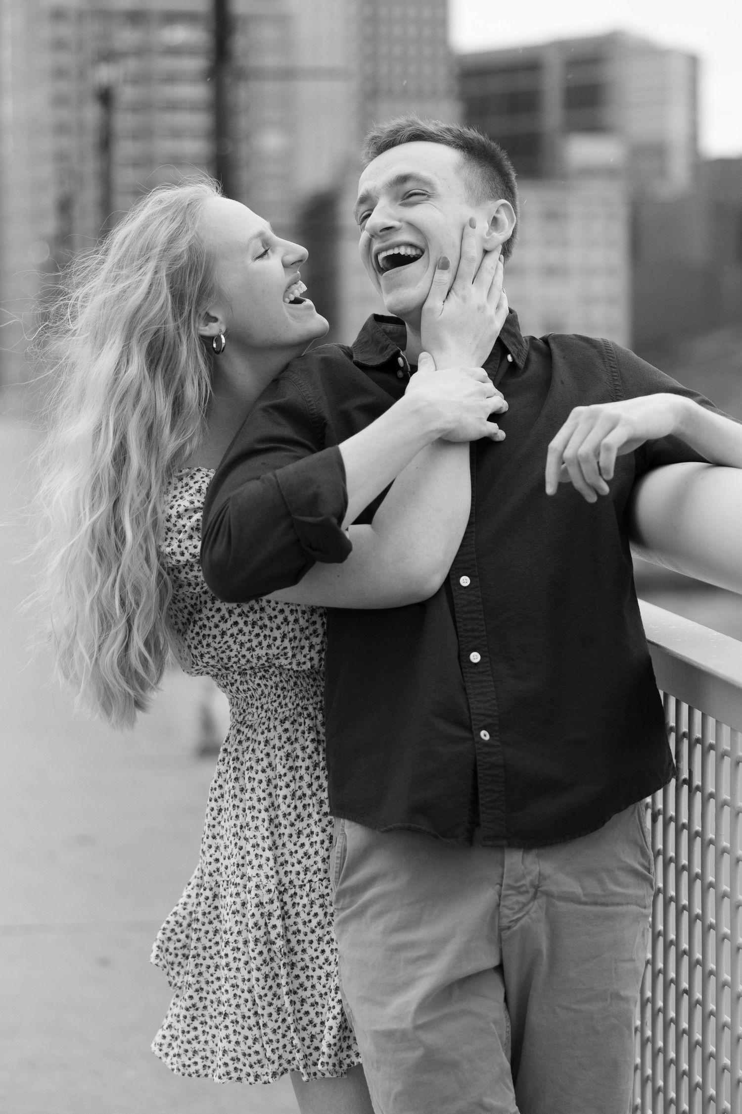 Couple laughing together on bridge deck in black and white engagement photo.