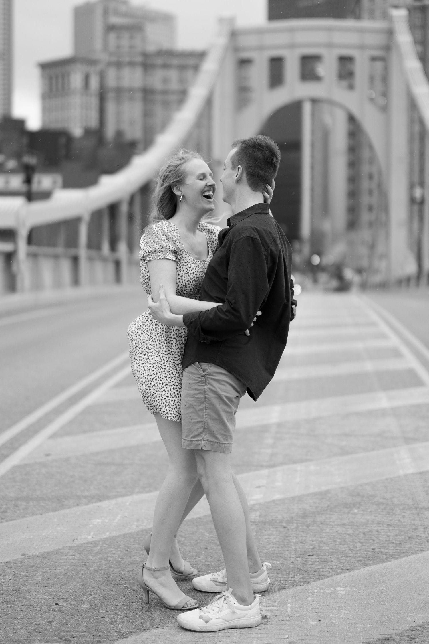 A romantic black and white moment captured of a couple embracing on a city bridge.