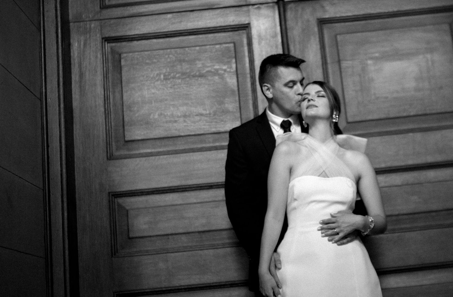 A black and white portrait of newlyweds against wooden paneling.