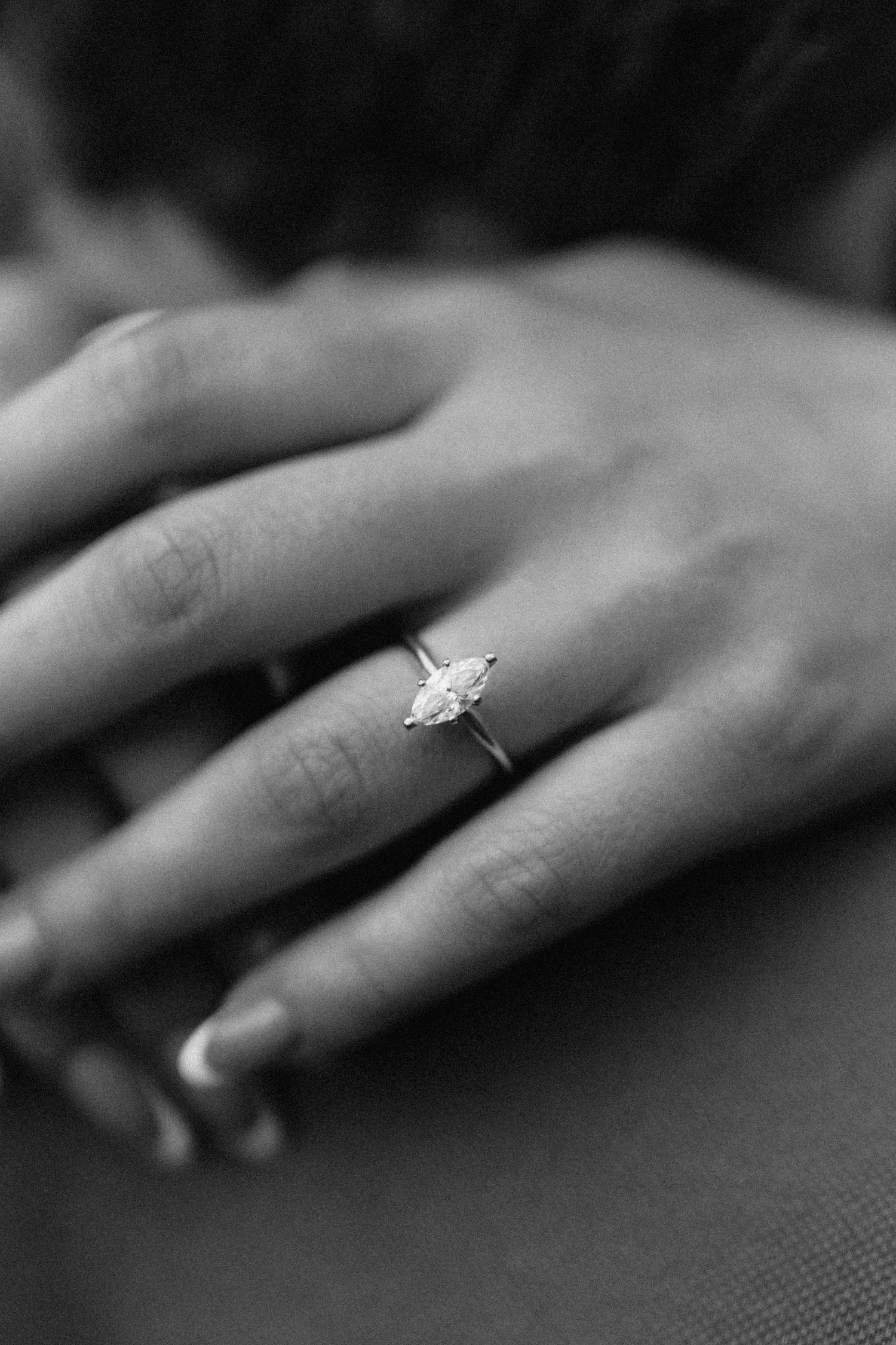A sparkling diamond engagement ring worn on a woman's delicate hand, captured in black and white.