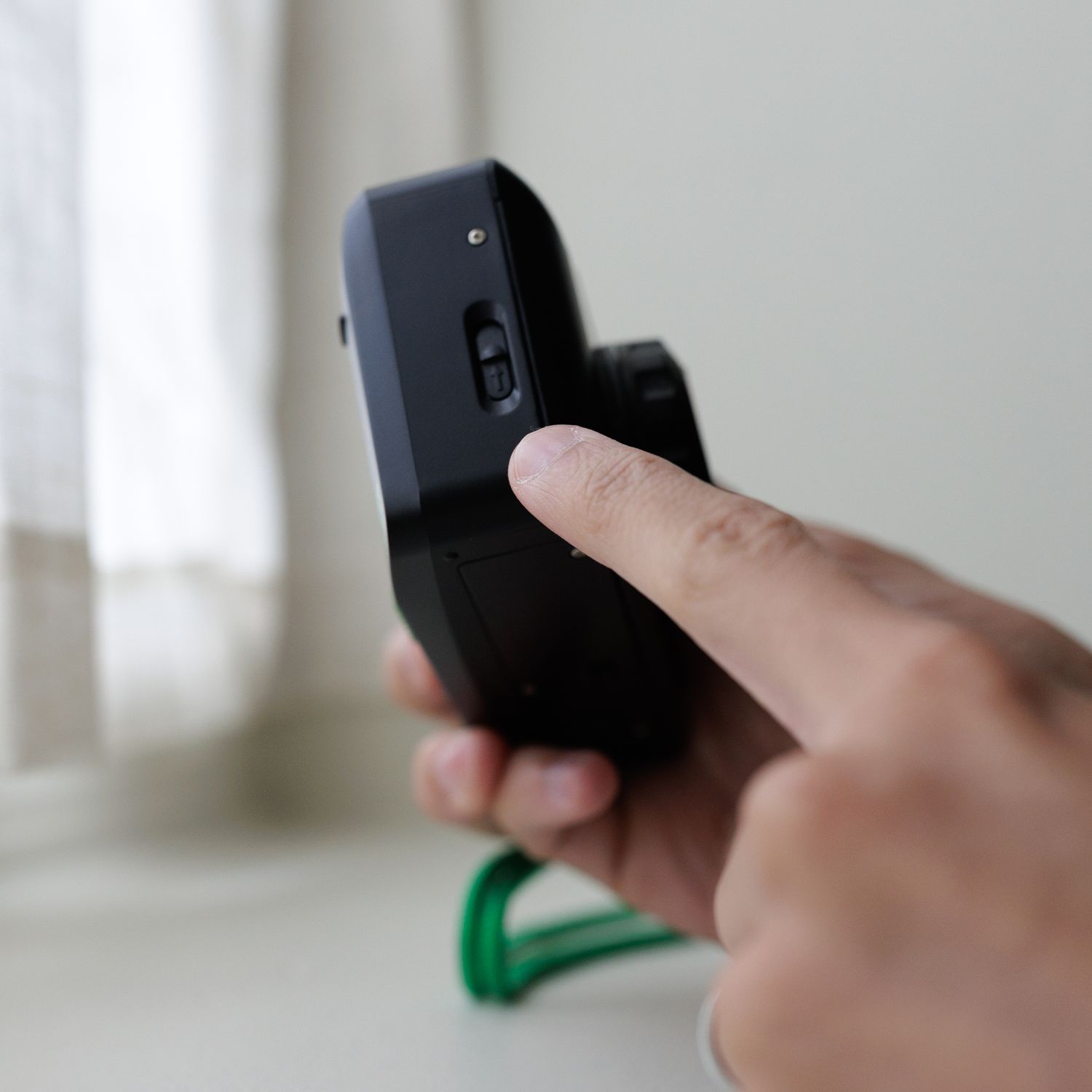 A blurred black smartphone or device screen is held in someone's hand in what appears to be a bright indoor setting.