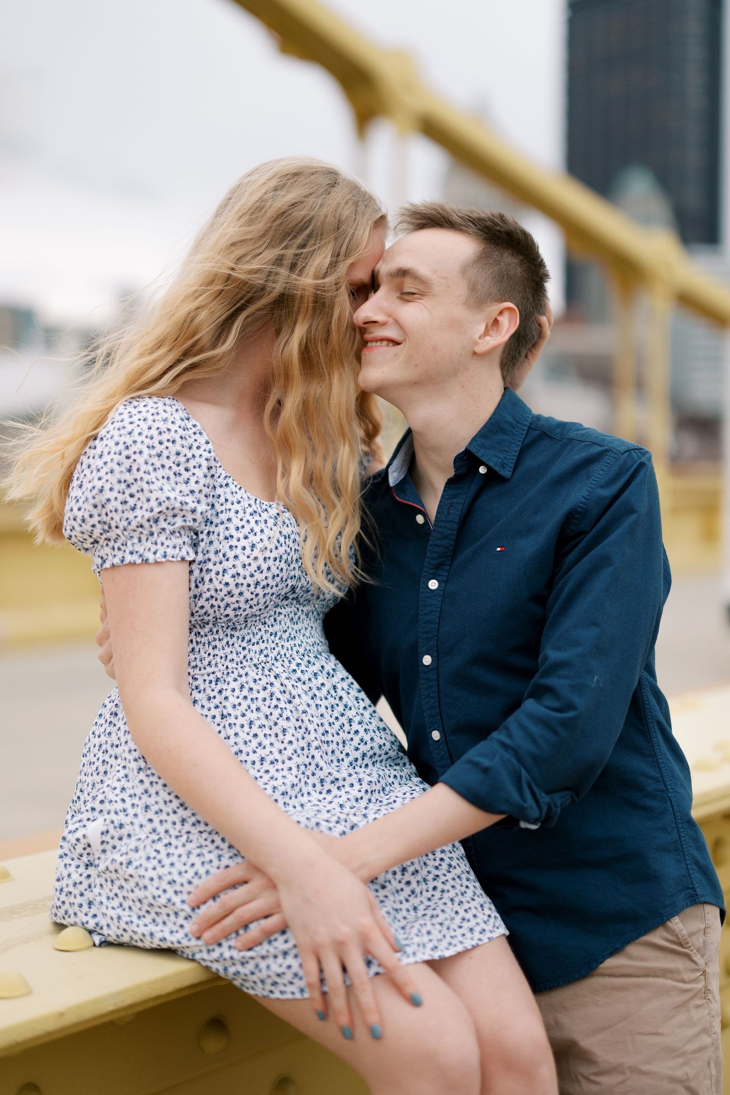 Couple sharing intimate moment on yellow bridge railing with city view.
