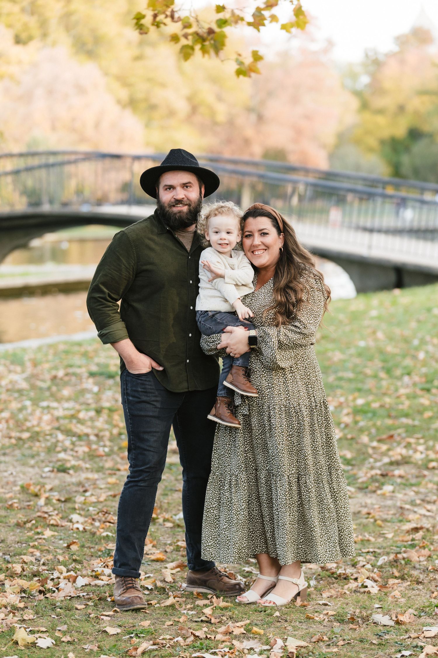 A family in coordinated fall outfits poses together on fallen autumn leaves in a park setting.