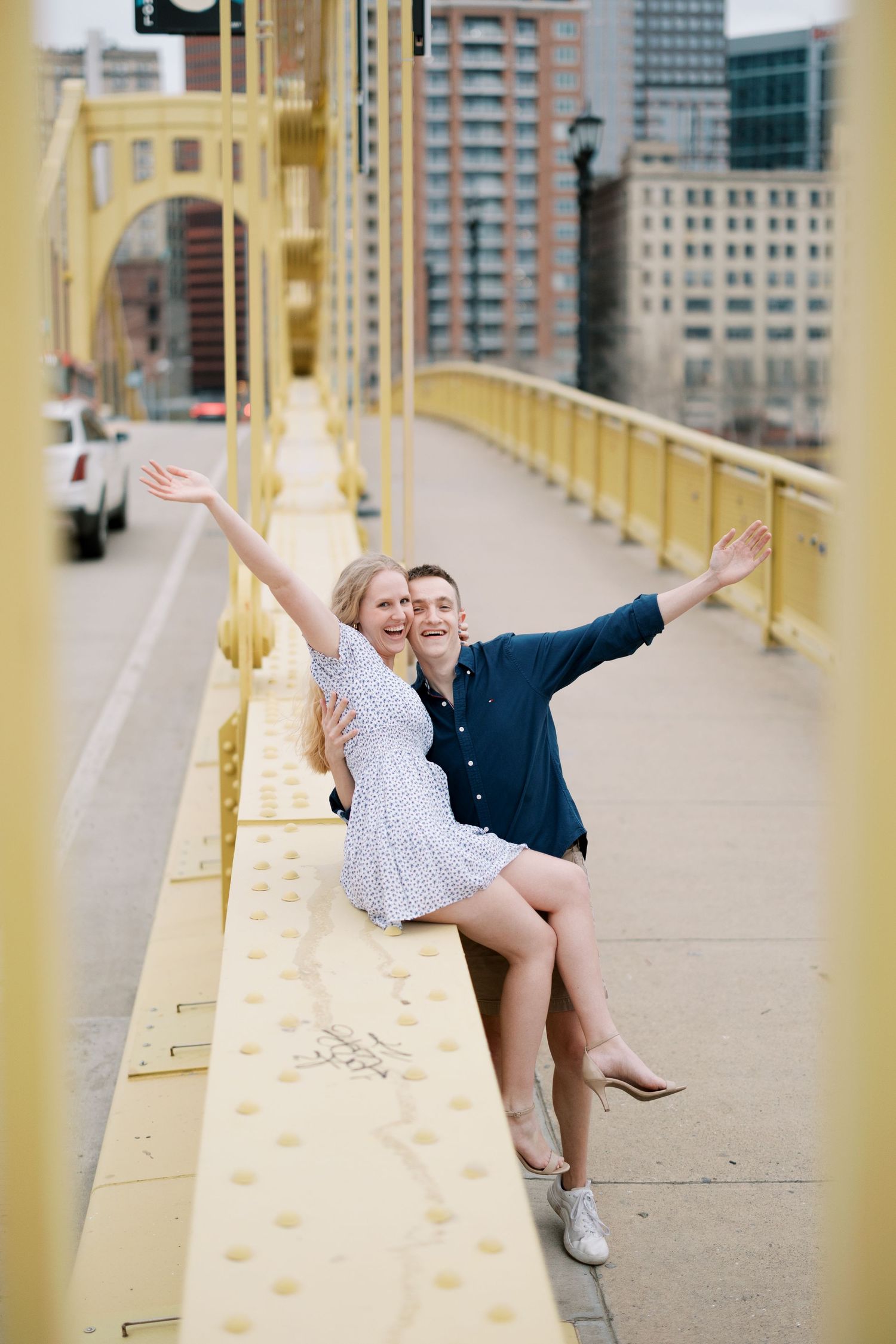 Couple poses playfully with arms outstretched on yellow bridge walkway.