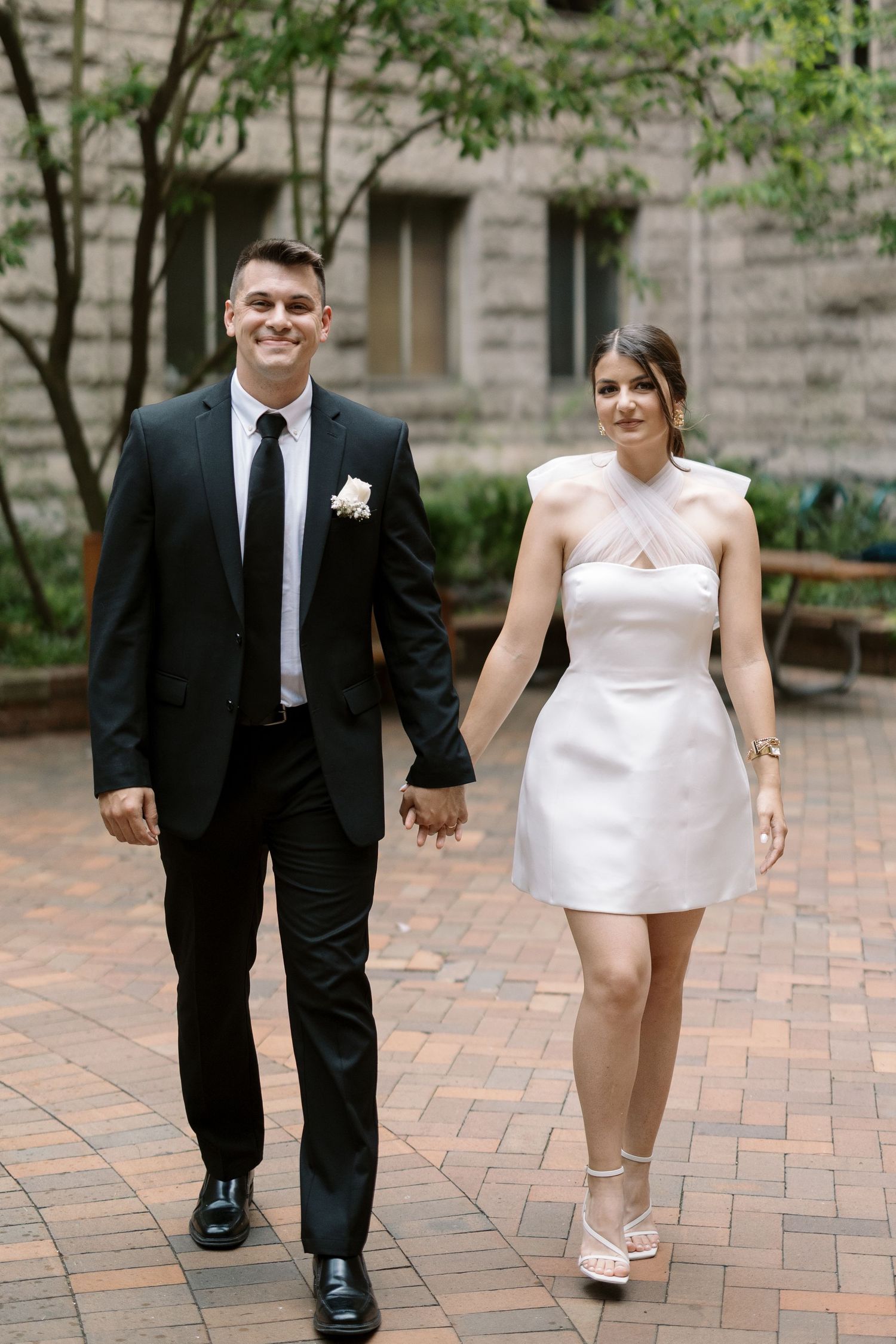A couple walks together on a brick path while holding hands and smiling.
