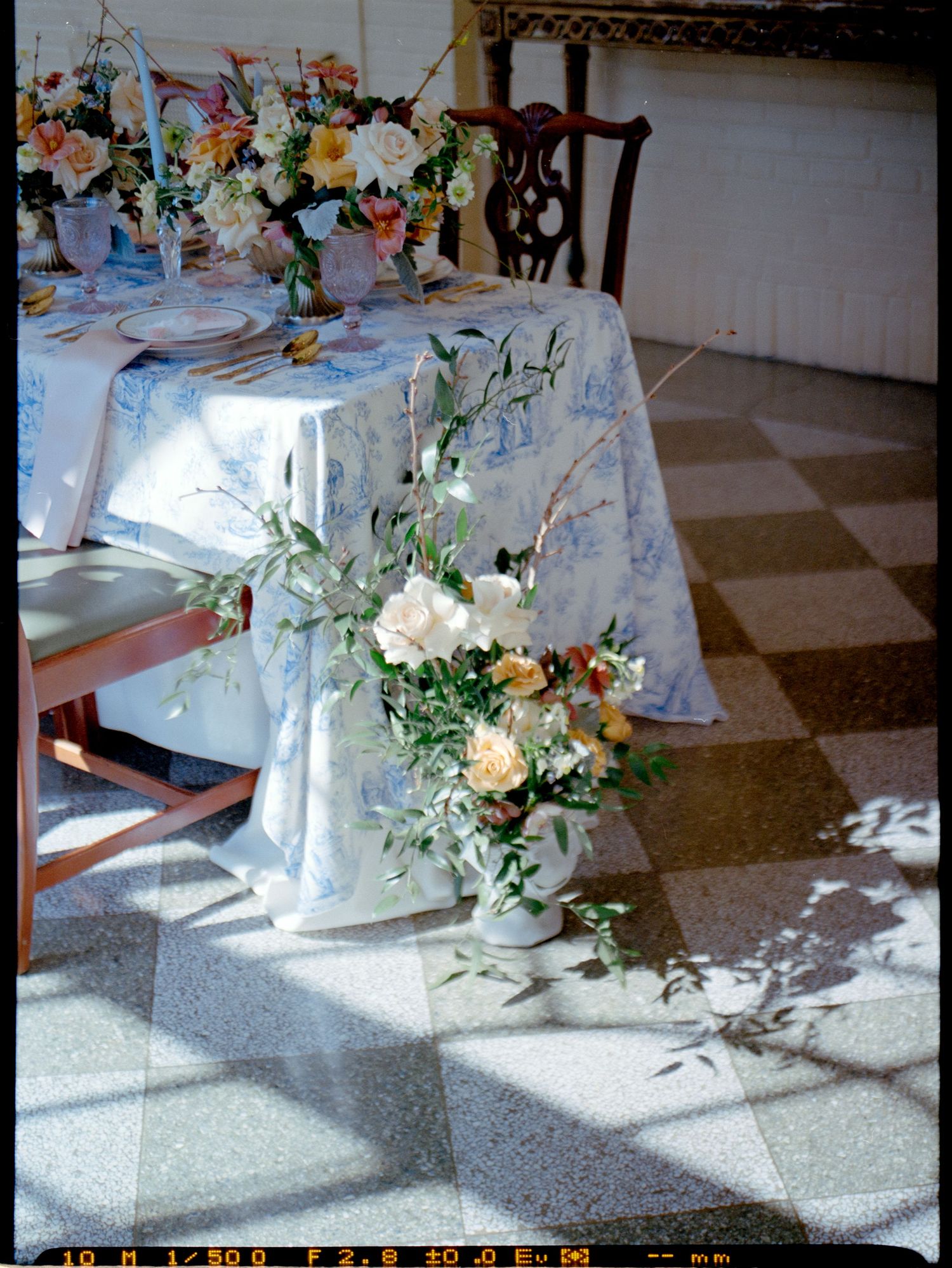 Elegant wedding table setting with floral arrangements and white linens in natural sunlight.