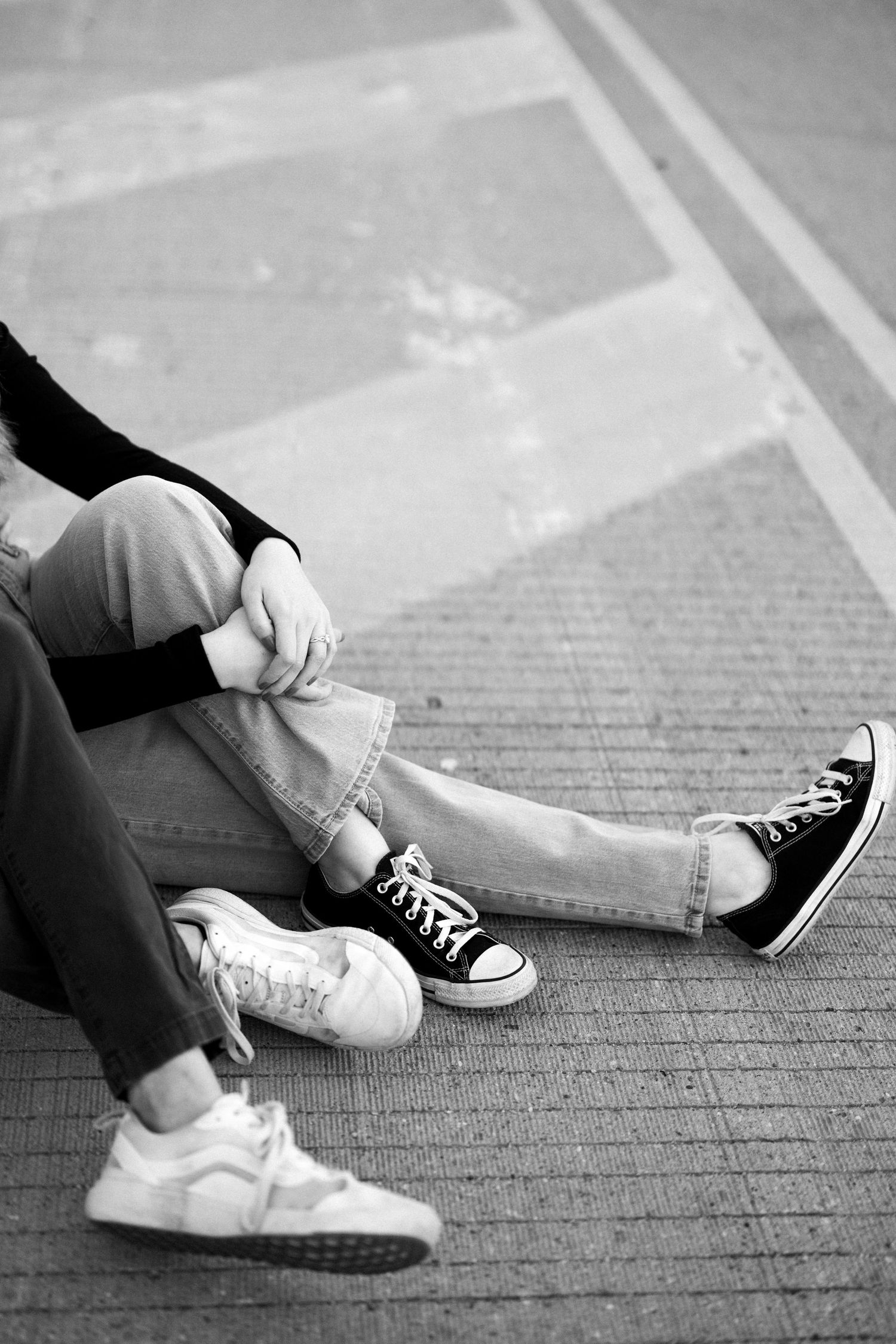 A black and white close-up of intertwined legs wearing contrasting sneakers.