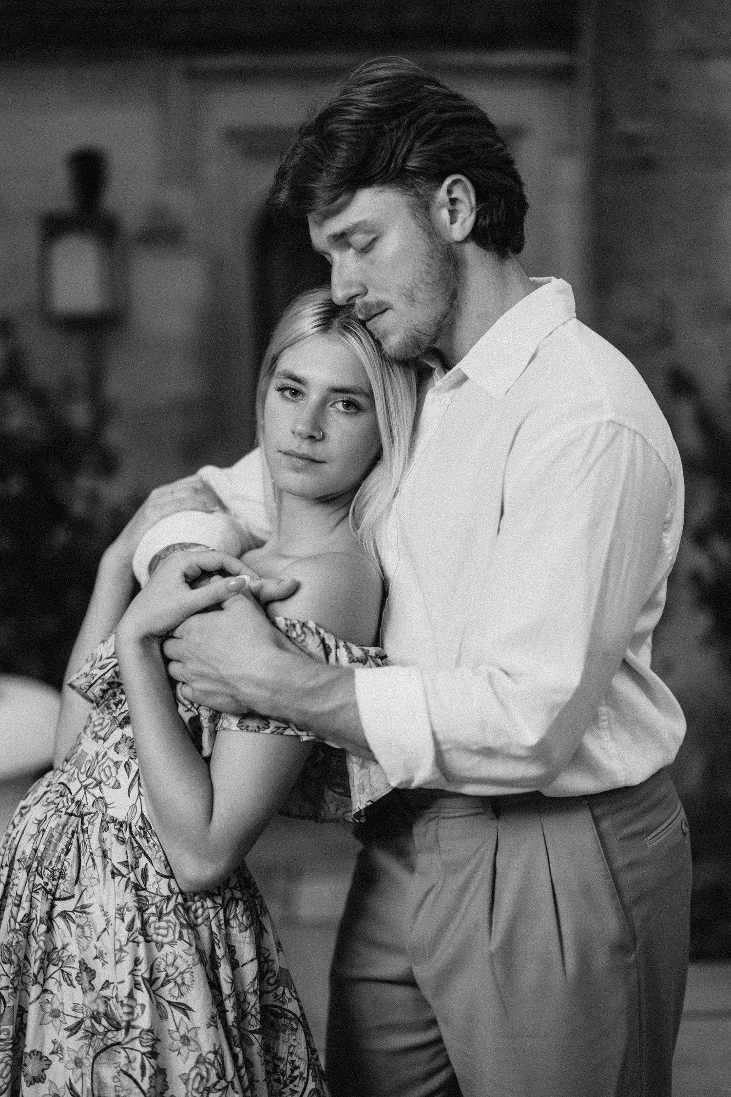 A romantic vintage-style portrait of a couple embracing in formal attire against a dark background.