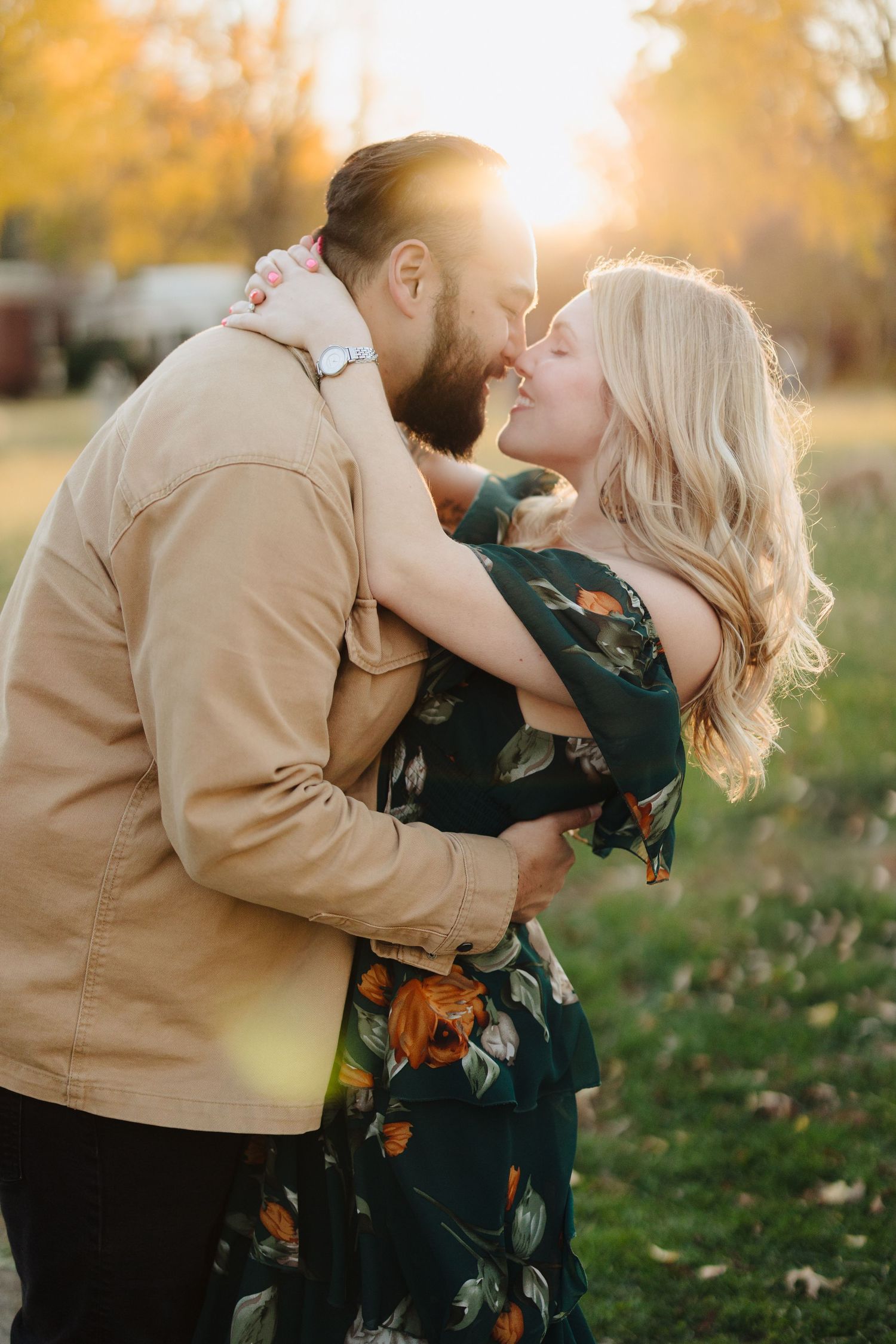 A couple shares romantic kisses while embracing during a golden sunset photo session in an autumn field.