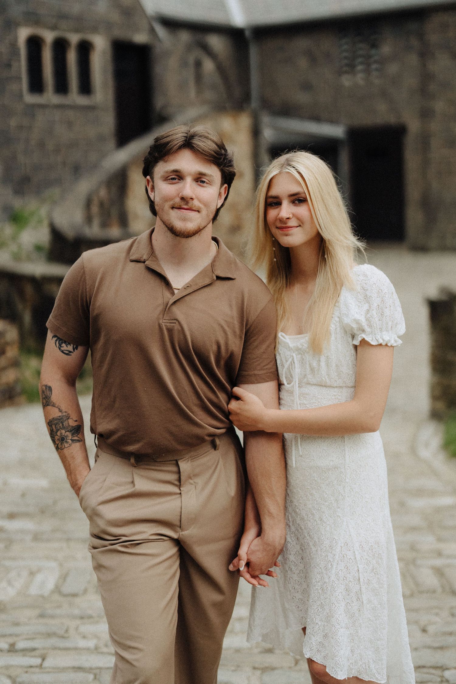 A couple poses together outside a historic stone church building.