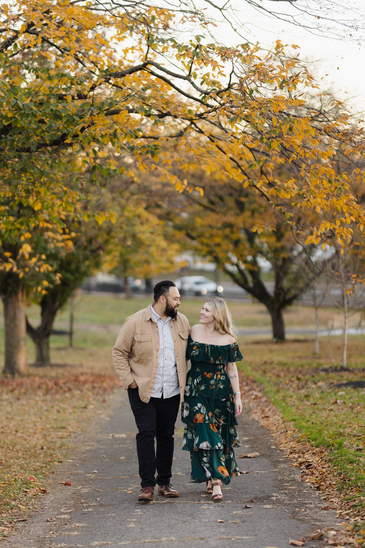 A couple takes a romantic stroll along a tree-lined path with golden autumn foliage overhead.