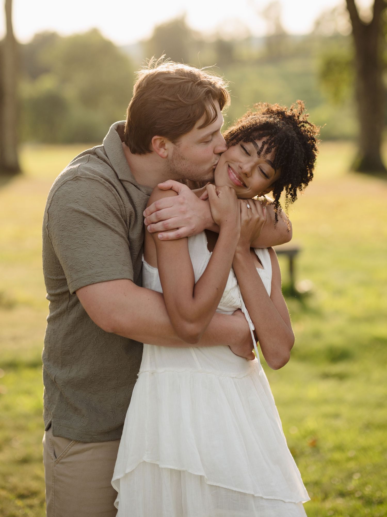 Romantic couple sharing a tender kiss outdoors in a grassy field during golden hour lighting.