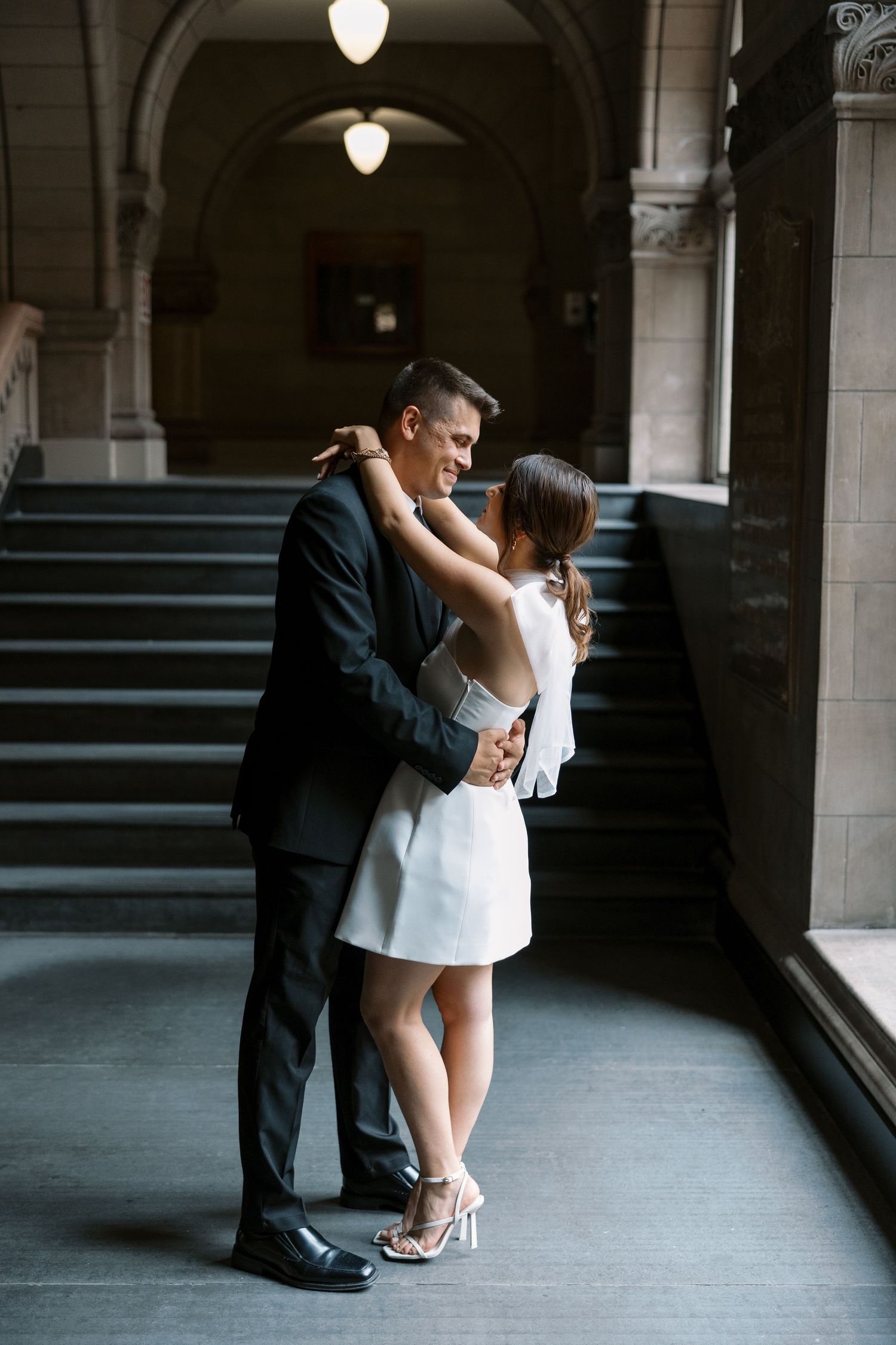 A romantic embrace captured between a couple in formal attire near a grand staircase.