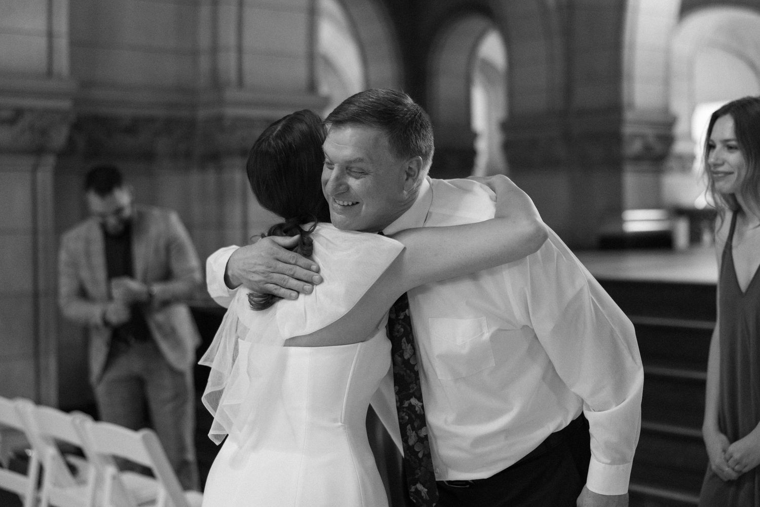 Black and white photo of wedding embrace in elegant stone building with arches.