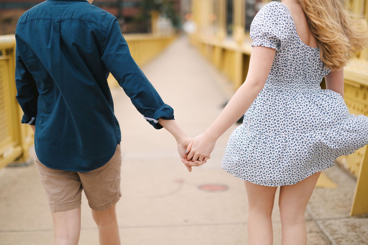 A couple holding hands while walking on a yellow bridge, showing their casual summer outfits.