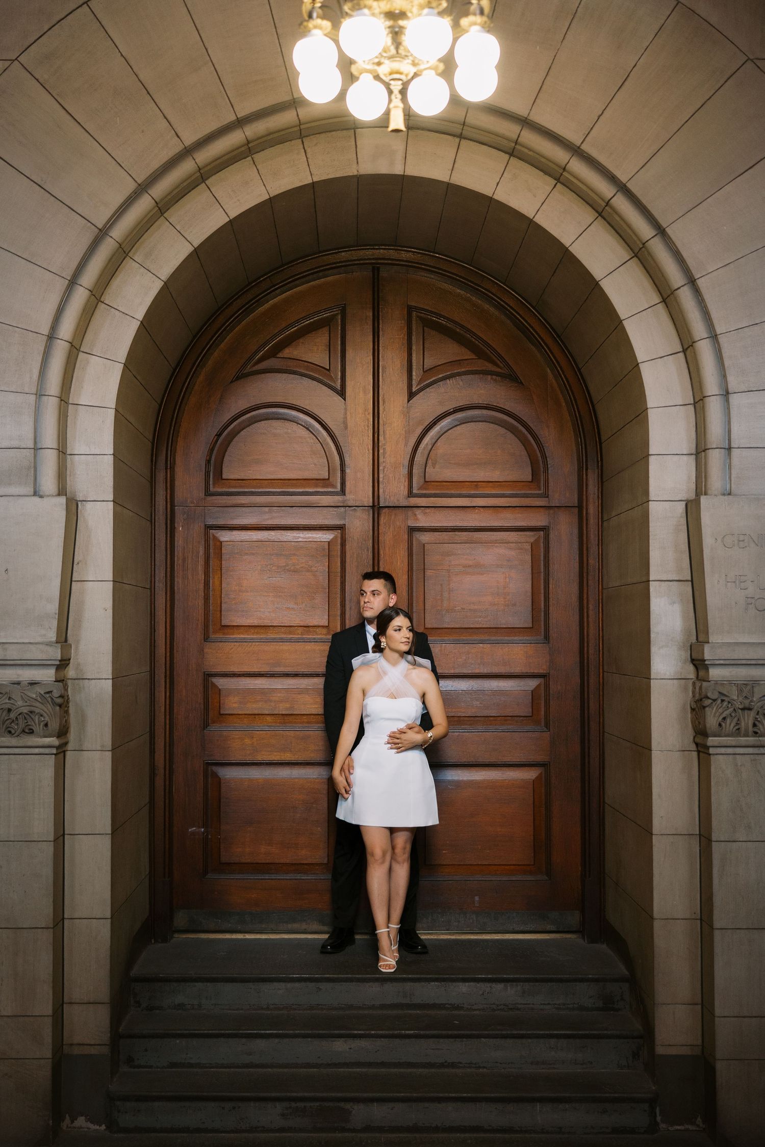 A couple stands in an arched doorway with beautiful architectural details.