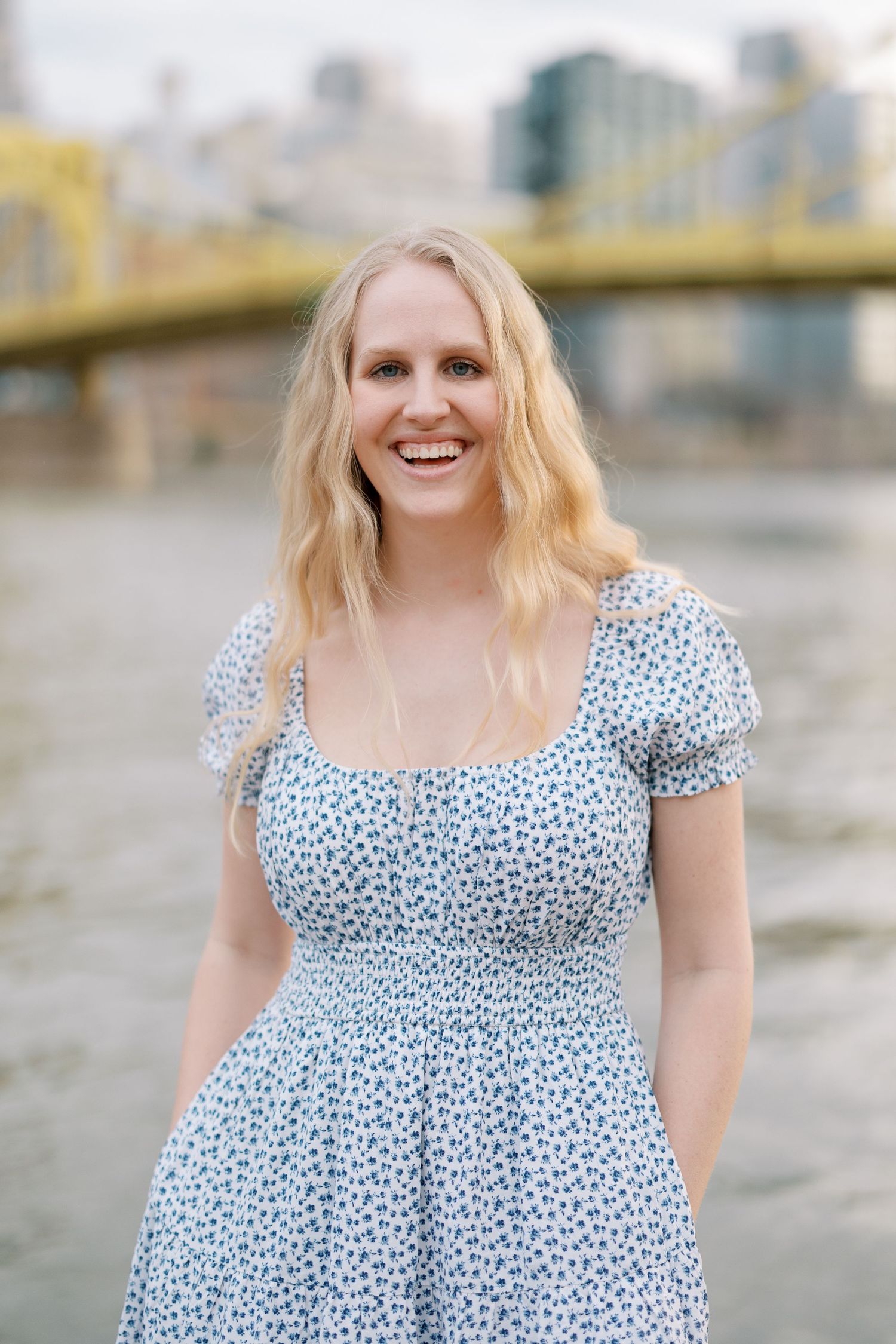 A portrait of someone in a polka dot dress smiling with a yellow bridge in the background.