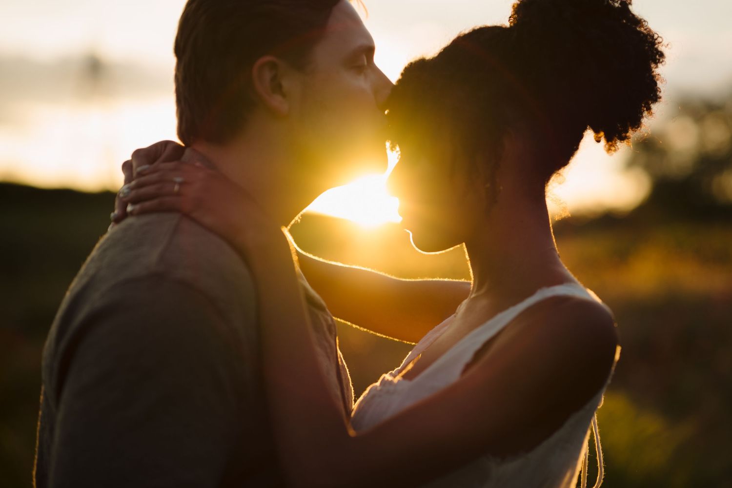 Silhouettes of a couple embracing outdoors at sunset with golden sunlight creating a romantic backlit effect.