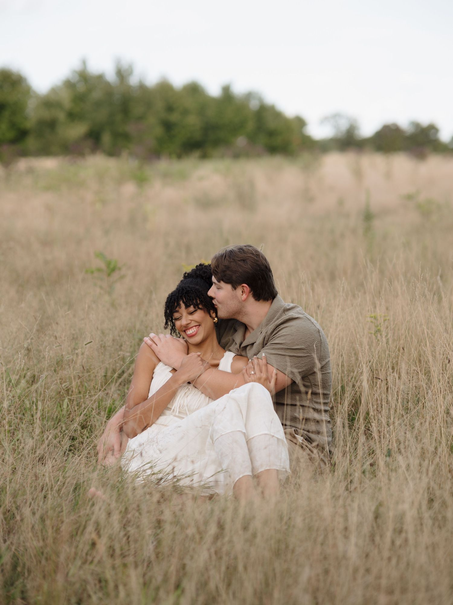 A loving couple lies together intimately in a sun-lit field of tall grass and wildflowers.