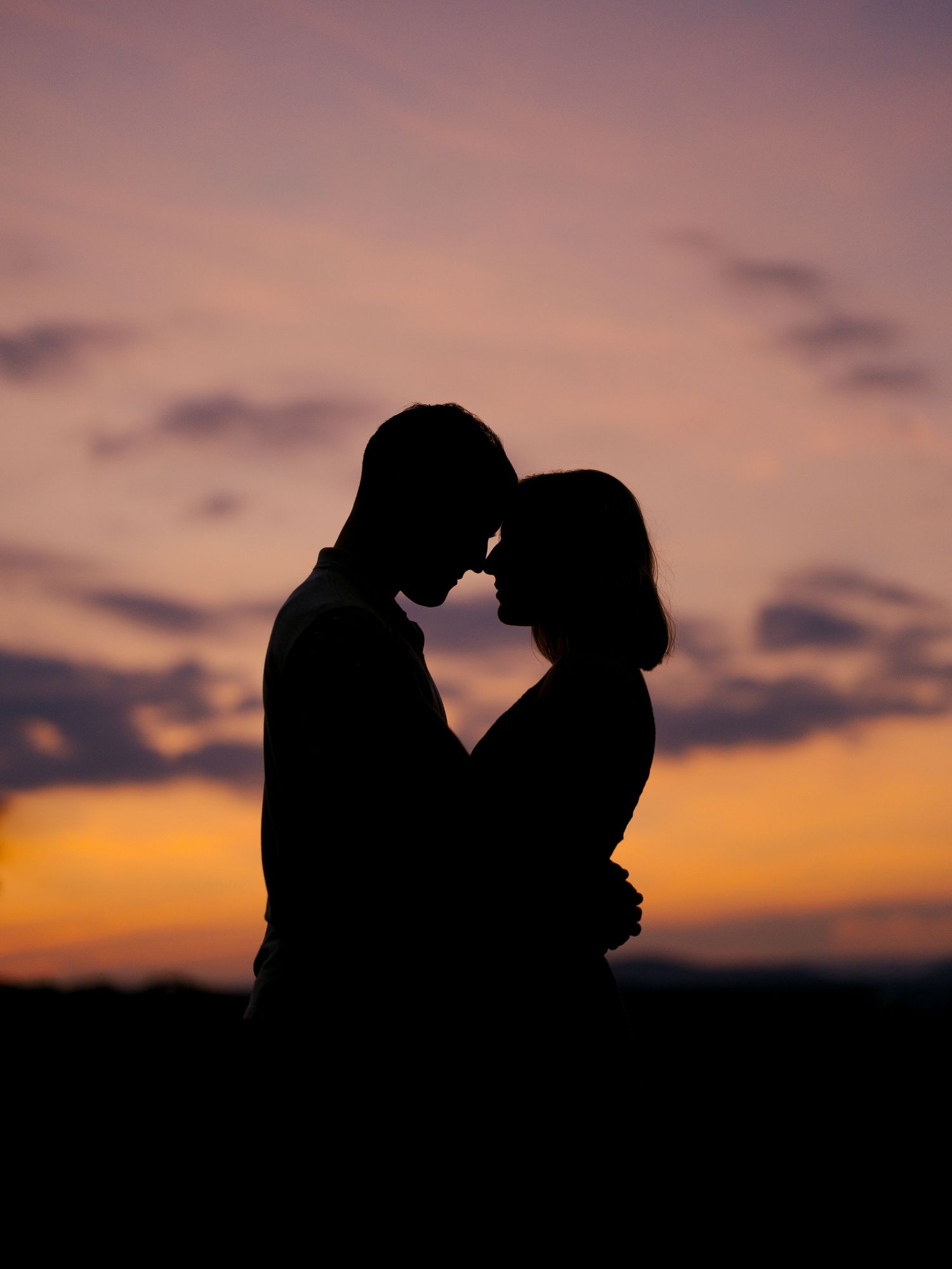 Silhouetted couple in romantic embrace against vibrant purple and orange sunset sky.