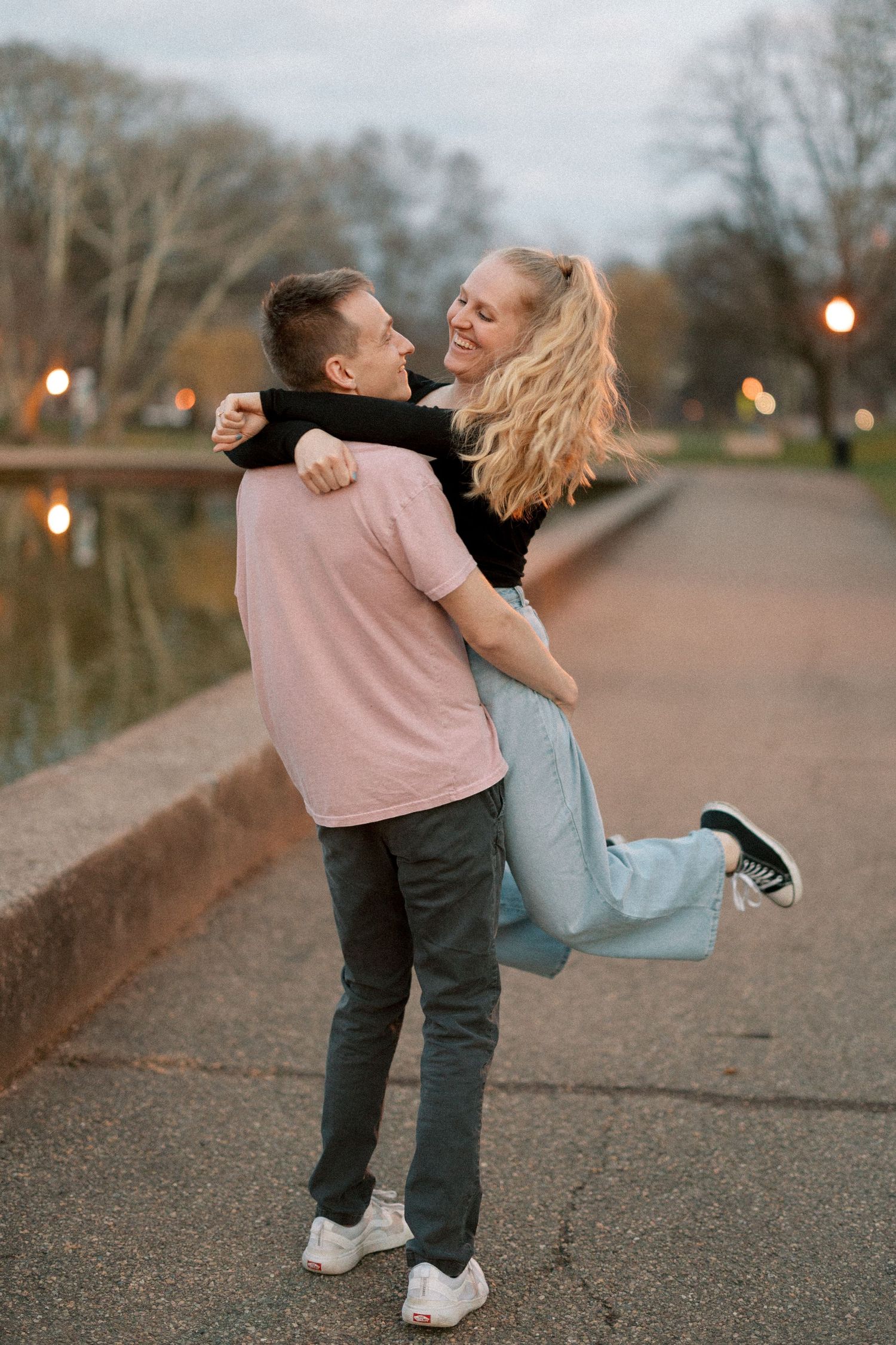 A playful moment captured between a couple on a path by a pond at dusk.