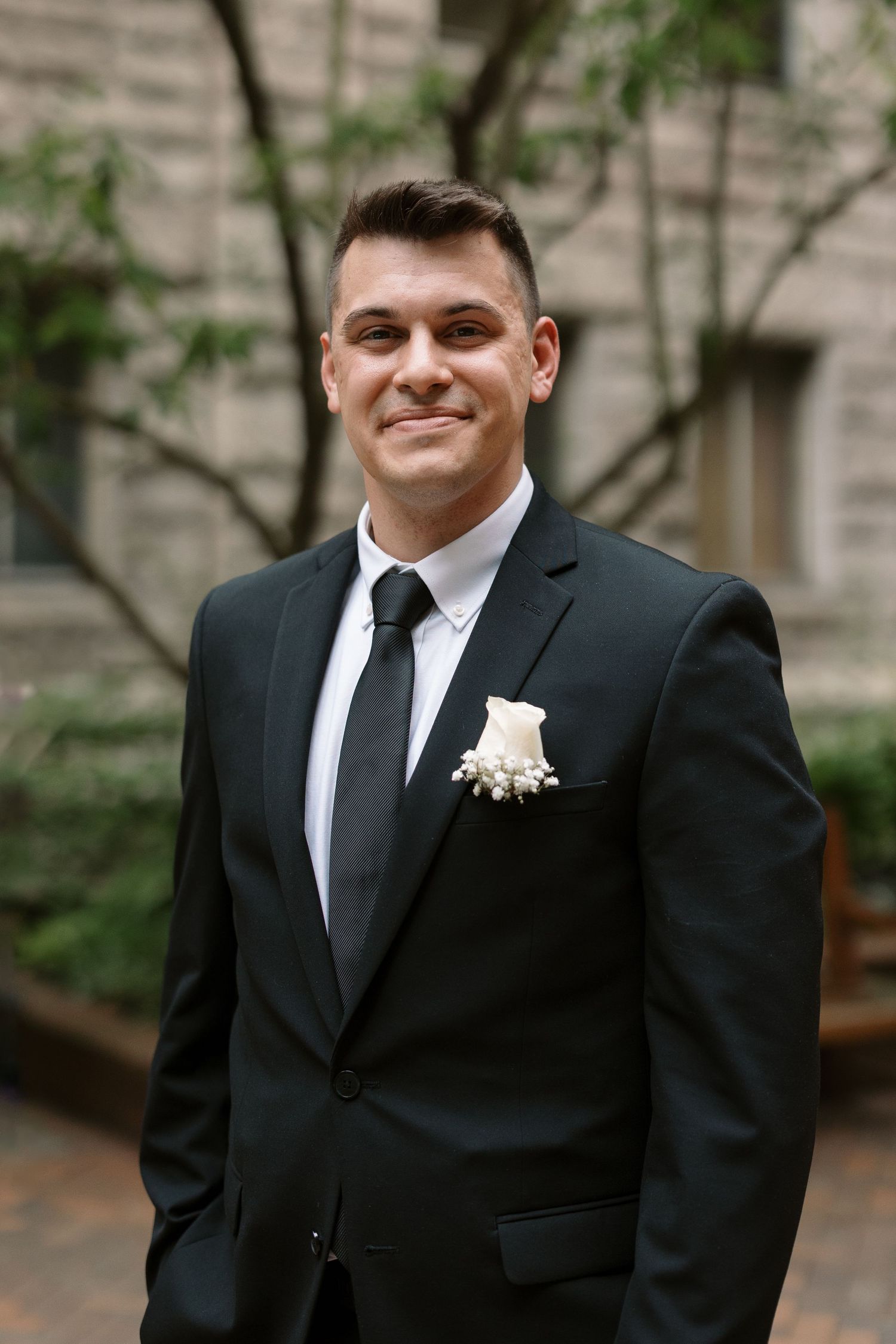 A formal portrait of a groom wearing a black suit and tie with a boutonniere.