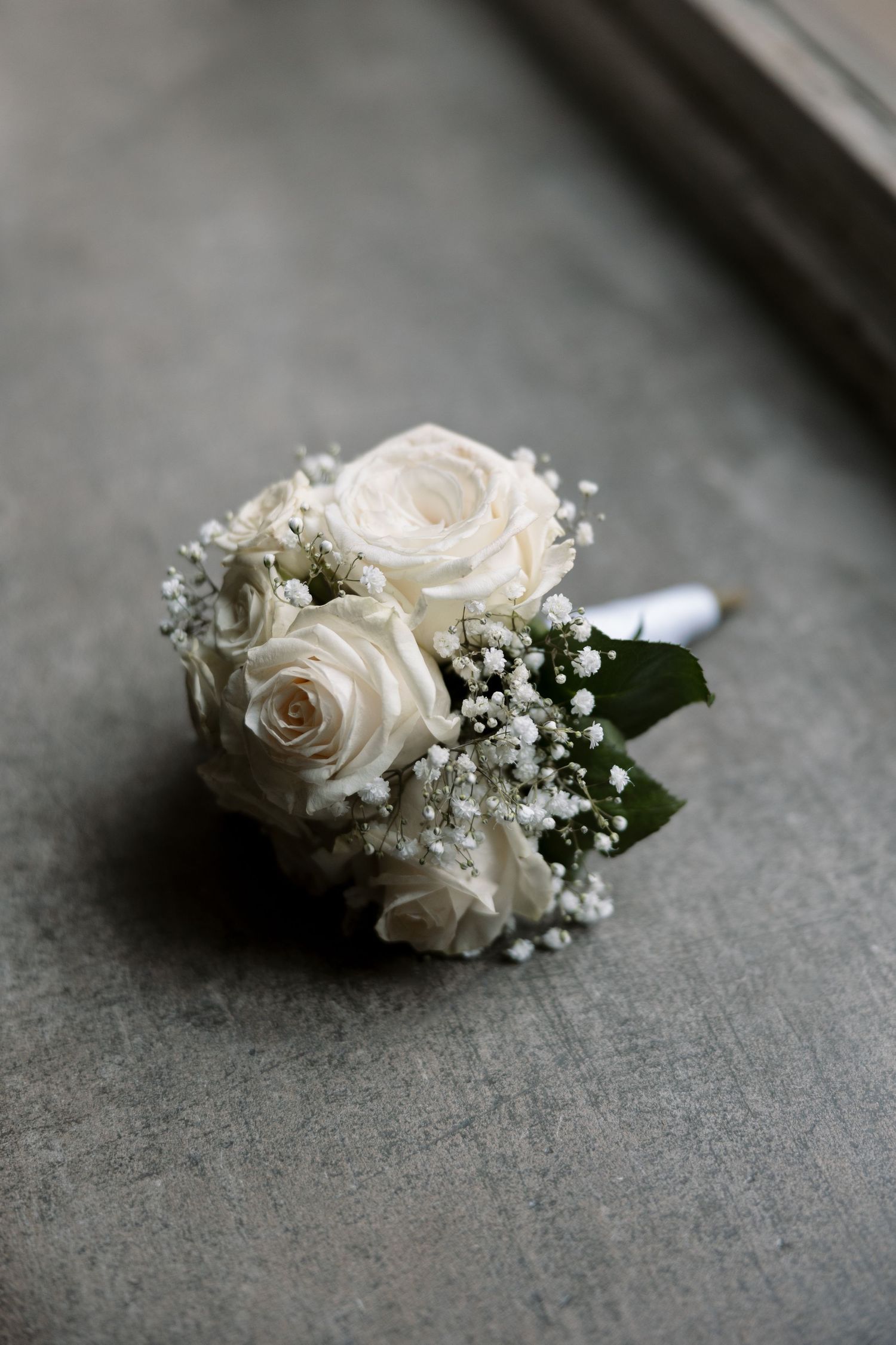 An elegant white rose and baby's breath bridal bouquet photographed on a gray surface.