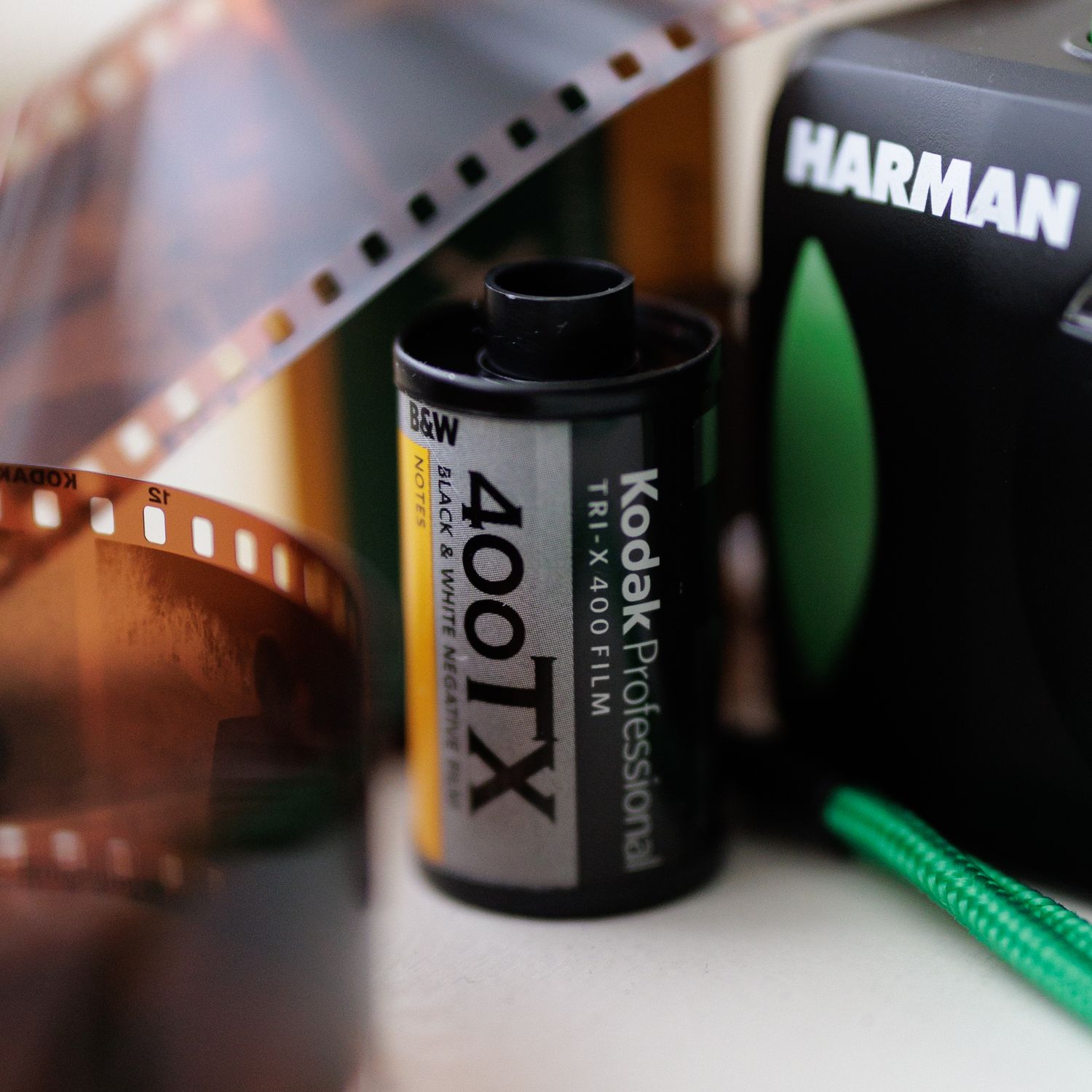 A roll of Kodak TMax 400TX black and white film next to Harman packaging with film strip in background.