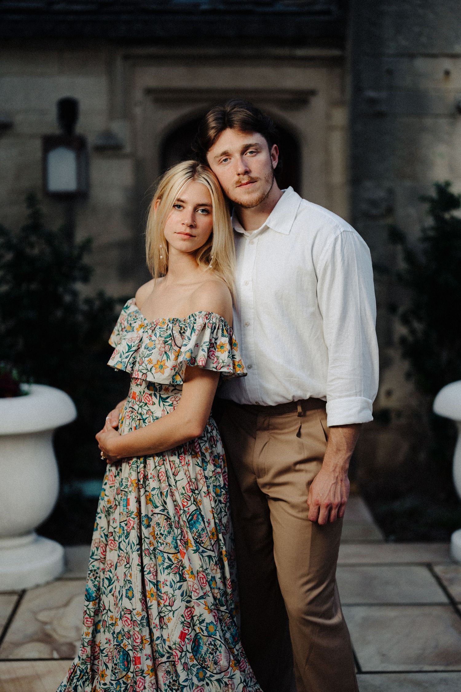 Couple poses together on stone patio with classical architecture backdrop.