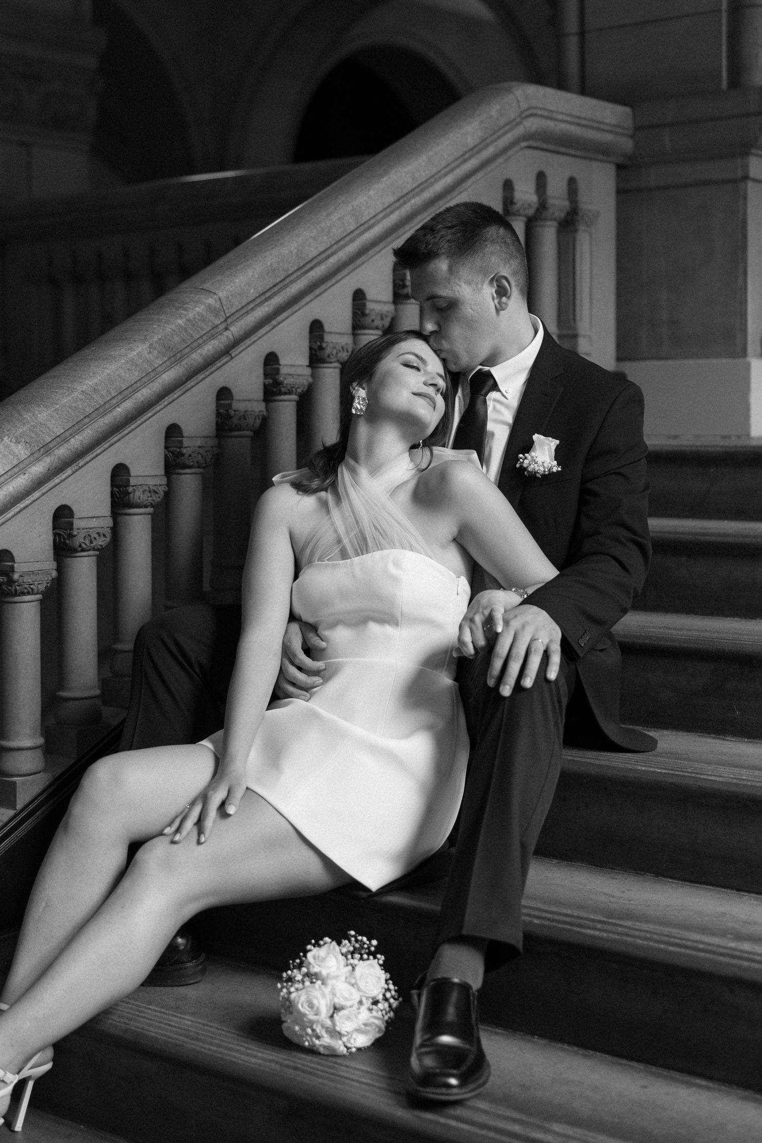 A black and white wedding photo capturing a tender moment on grand stone steps.