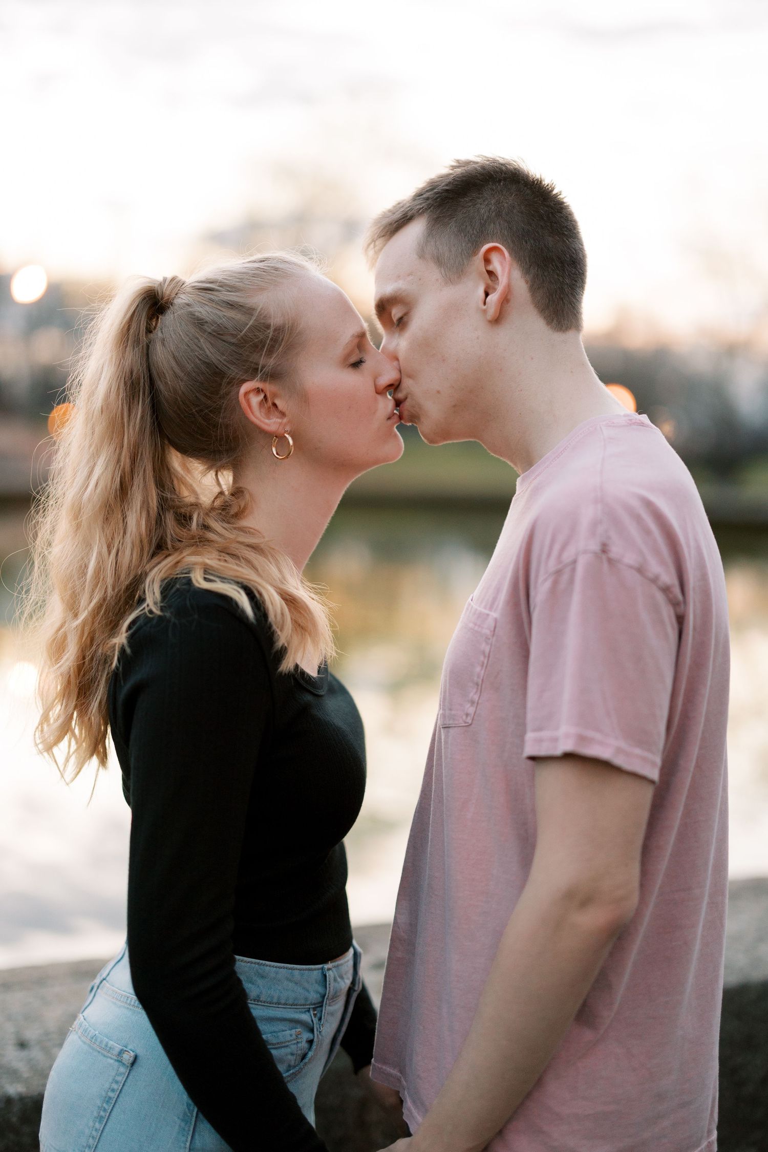 A romantic moment captured at sunset beside a pond in a park.